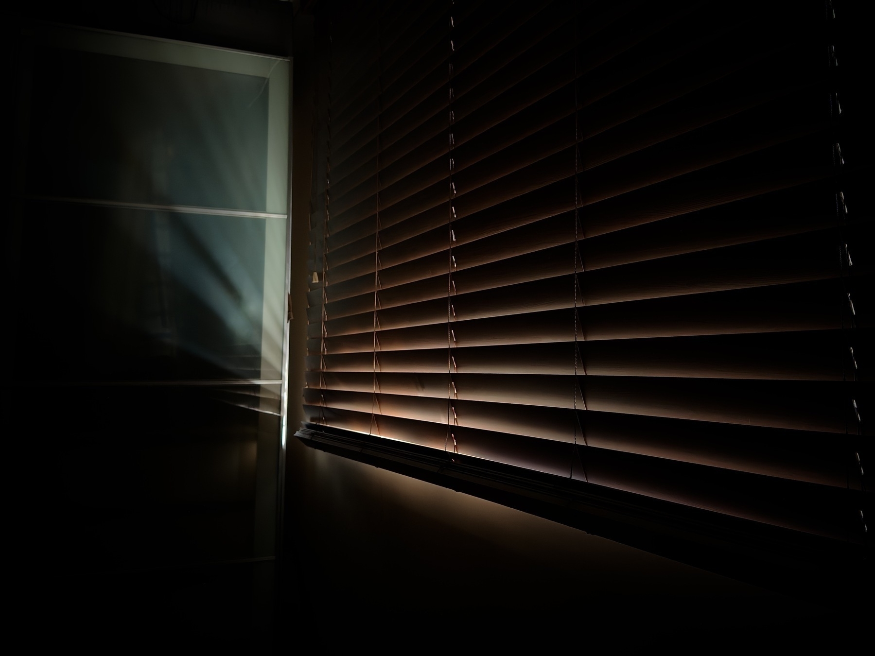 Morning light sneaks through closed wooden slats, hitting the edge of a wardrobe.