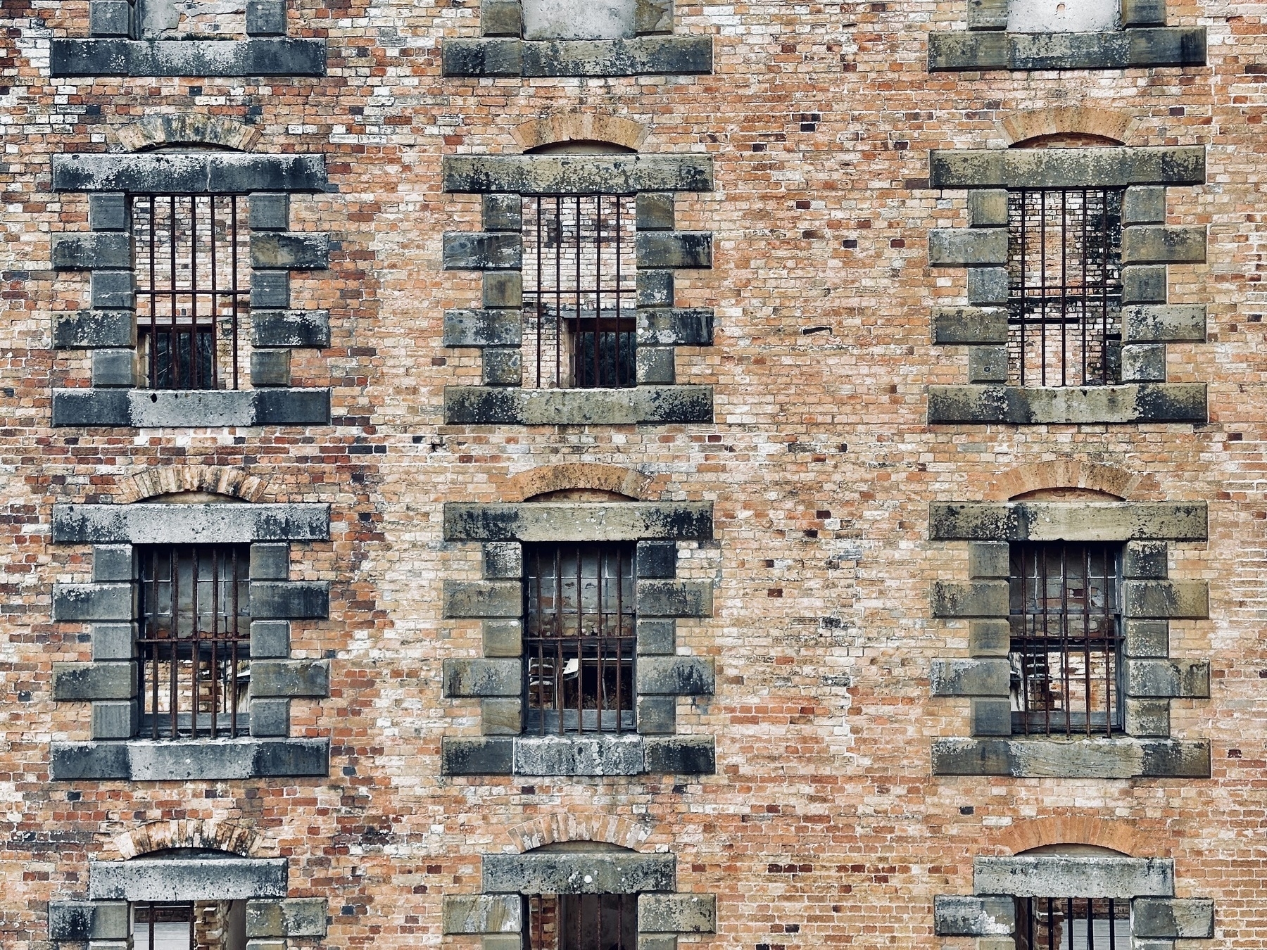 A red brick wall with several old gaol cell windows.