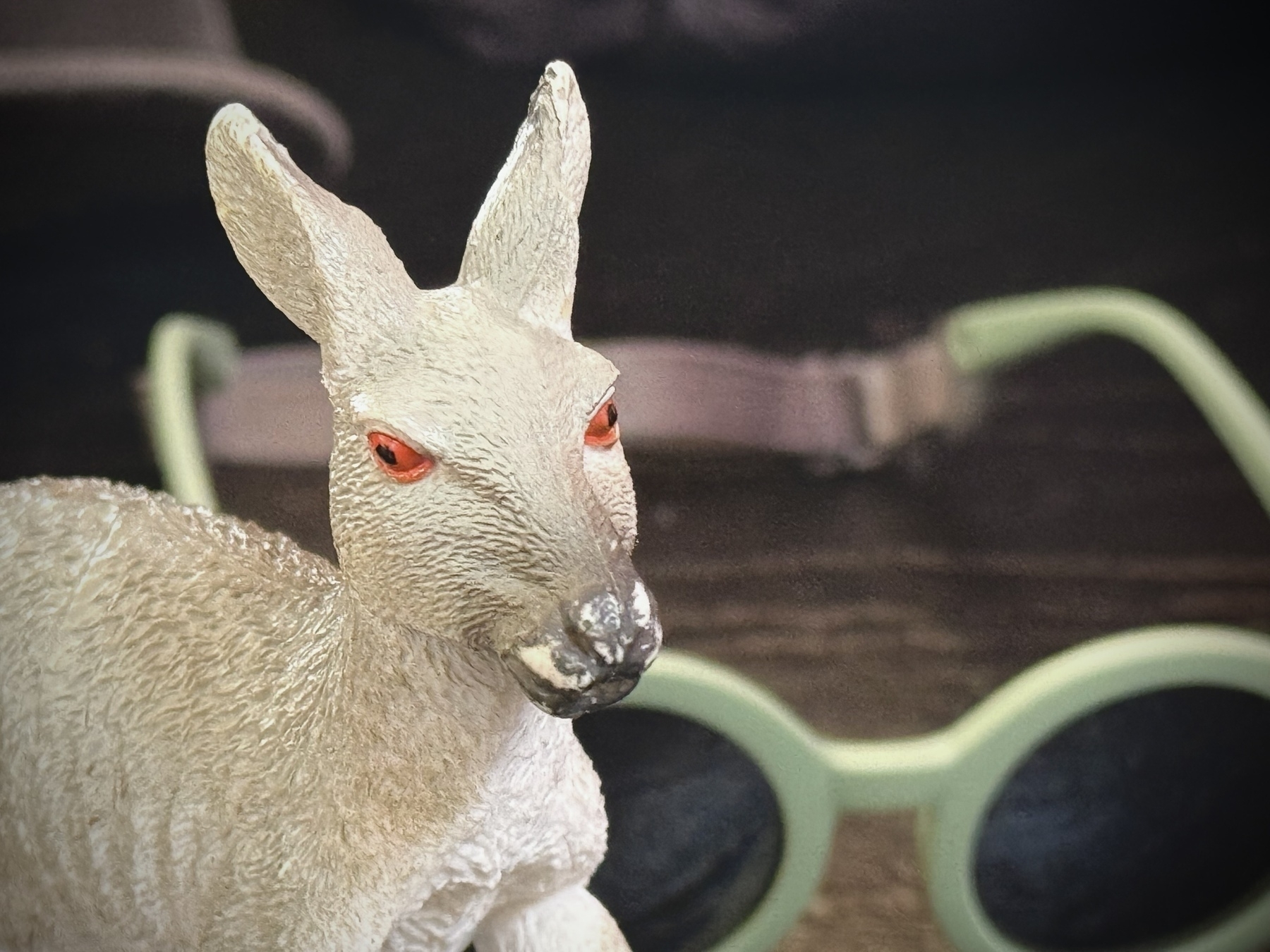 A small, detailed sculpture of a kangaroo with reddish eyes is placed in front of green-framed sunglasses.