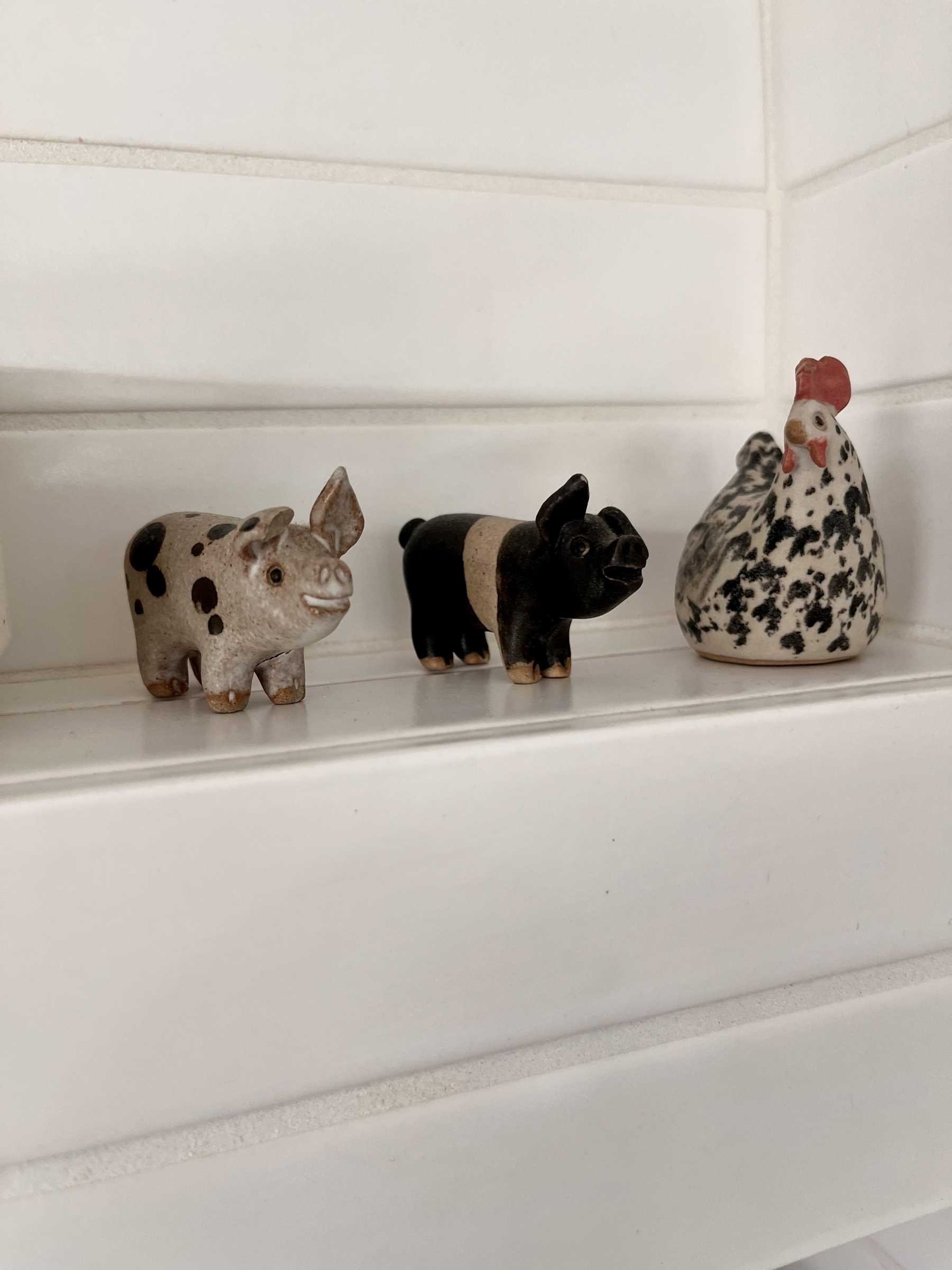 Two small china pigs and a hen on a shelf in a corner of our kitchen