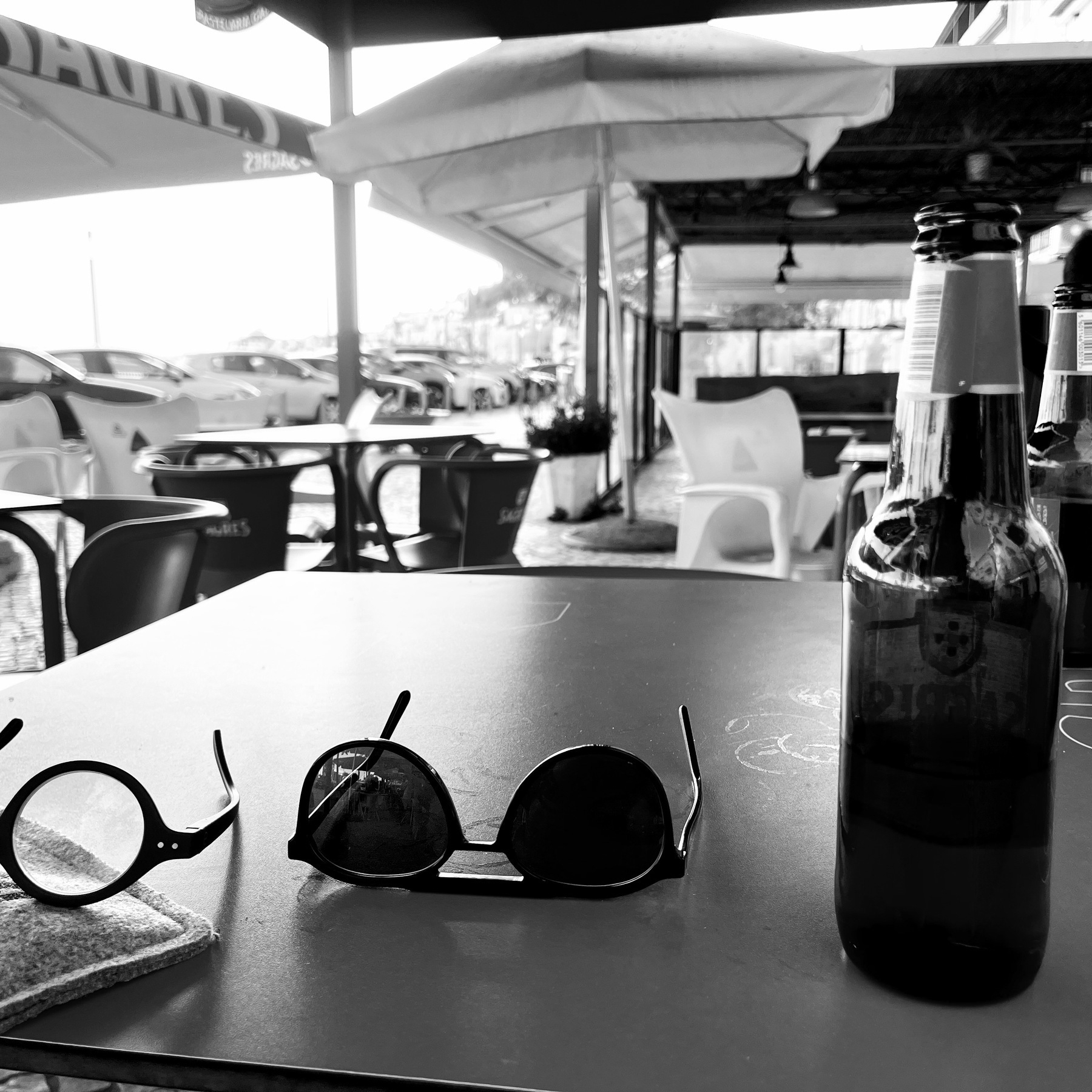 Black & white photo of a table with beer bottle, sunglasses and ordinary glasses on