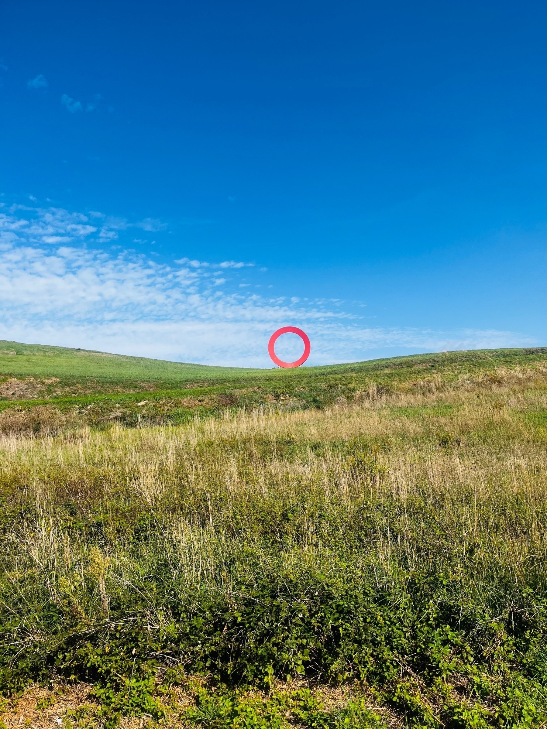 A large red metal circle standing upright in the middle of a field in Volterra, Italy