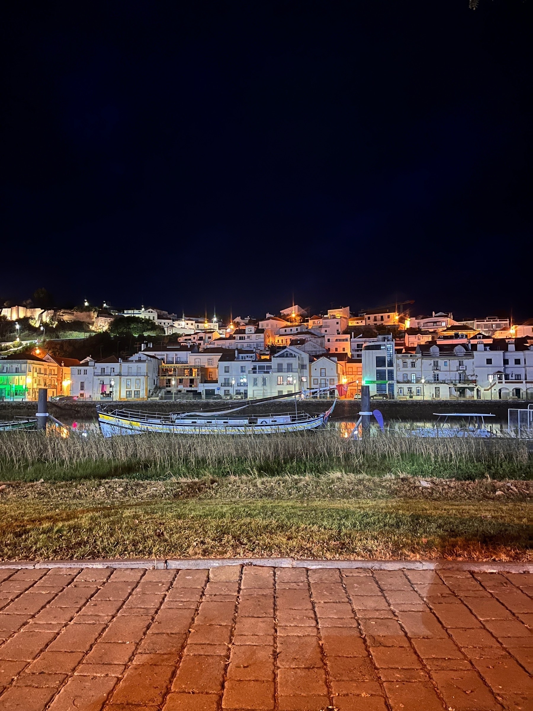 Alcacer do Sal at night, taken from the far bank of the River Sado, with a boat in the foreground