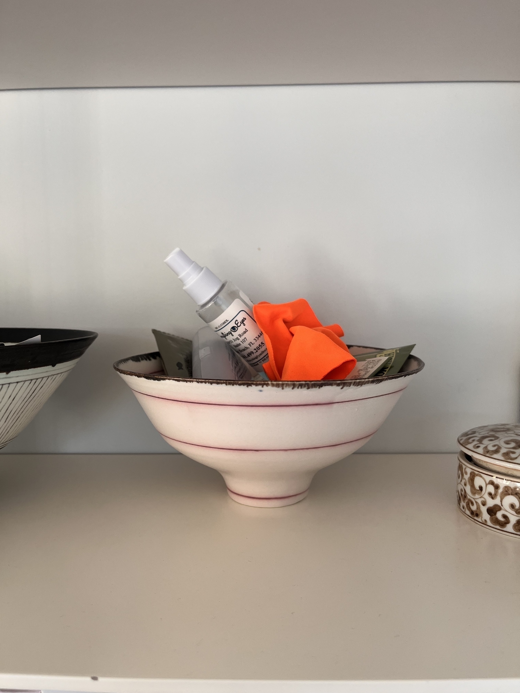An orange cloth, along with other items, in a china bowl on a shelf