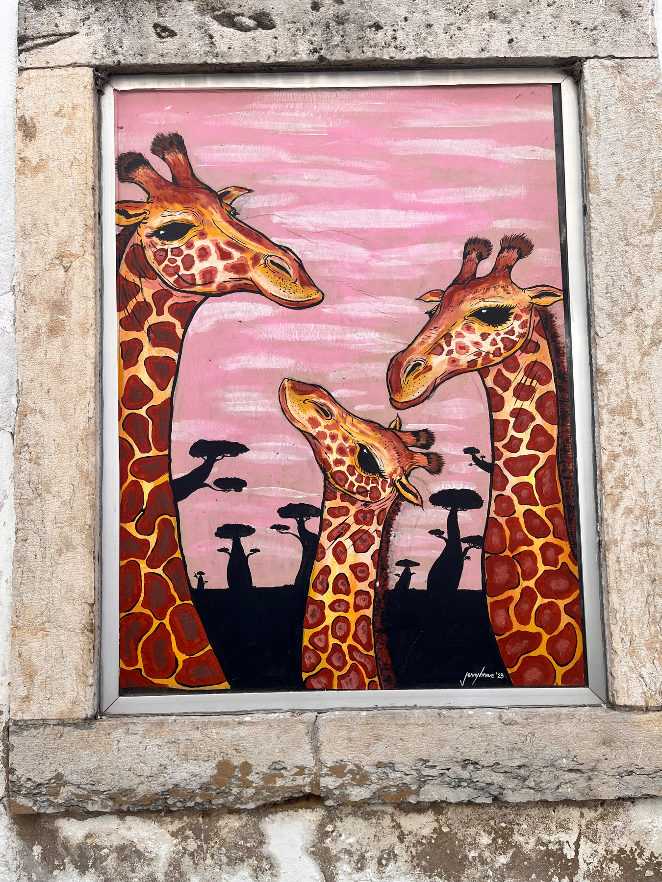 A vibrant painting on an outside wall of three giraffes against a pink background with silhouettes of tree