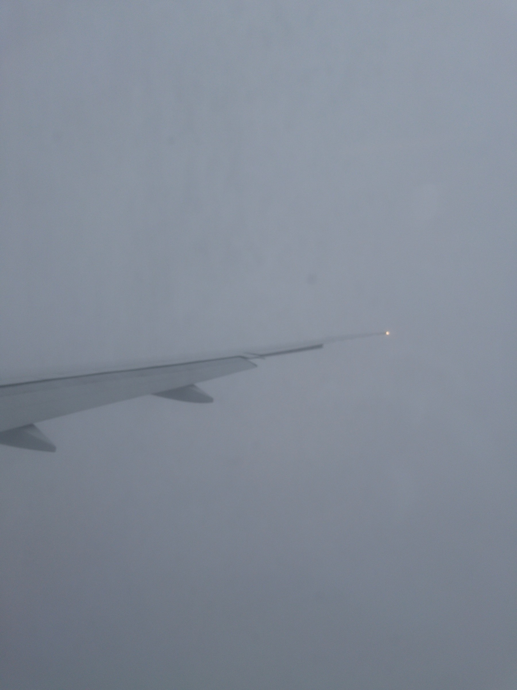 A view of an airplane wing from the window of the plane. The wing is surrounded by thick cloud less than a thousand feet over east London as an airplane comes into land.