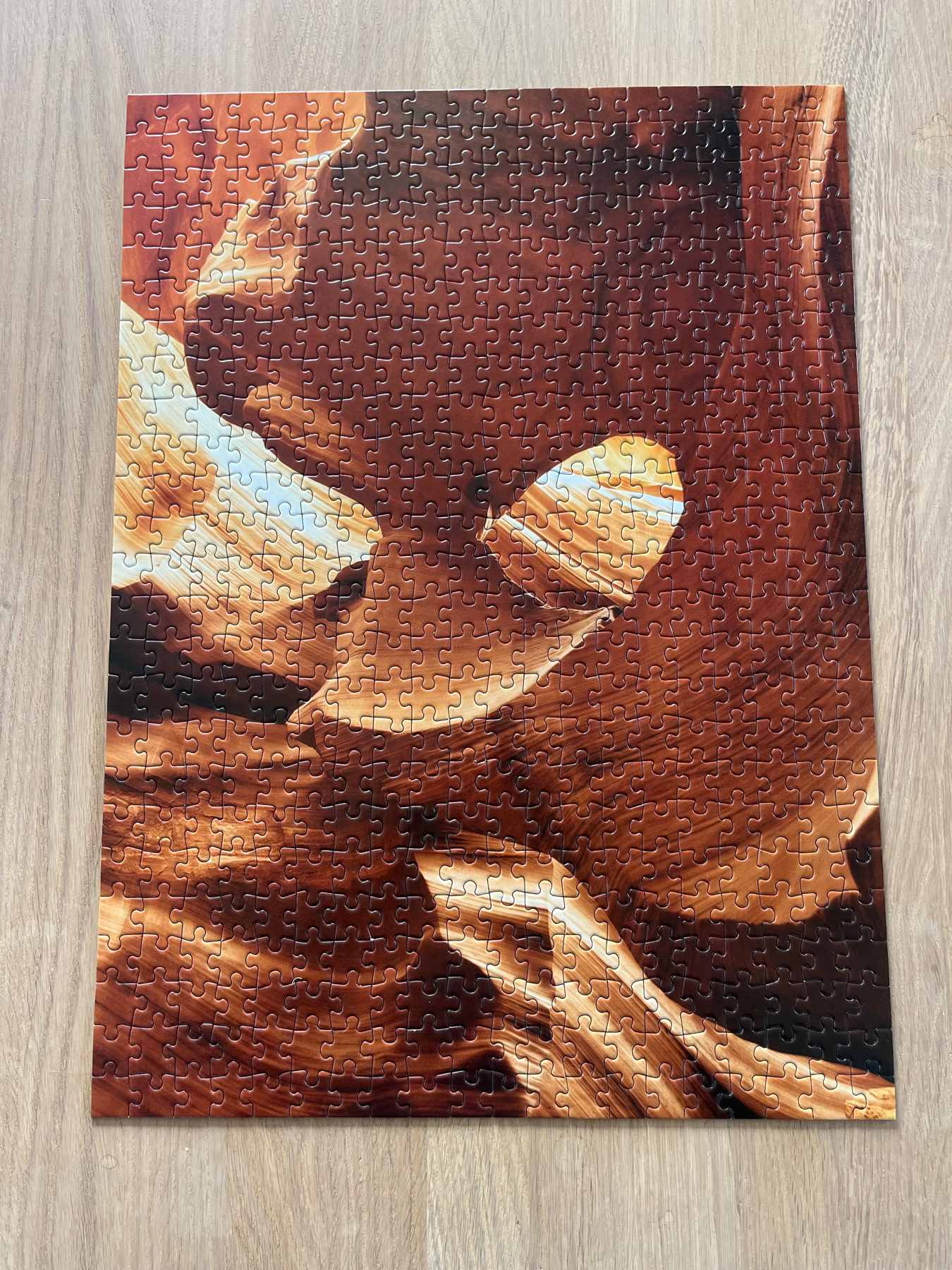 A 500 piece completed jigsaw puzzle on a wooden table. The puzzle is of rocks in different shades of browns, blacks and whites. 