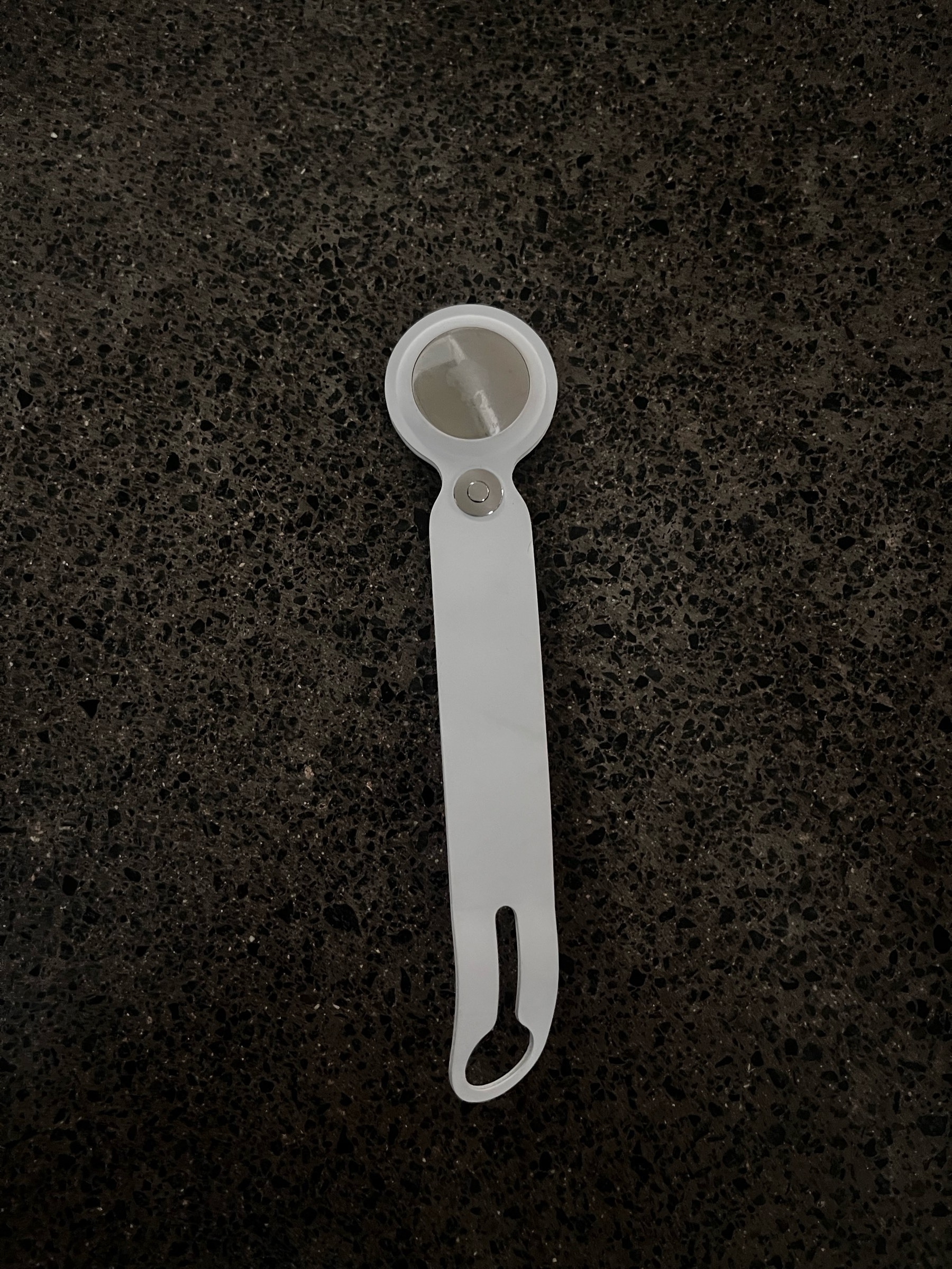 A white plastic tool with a circular end and a slit at the handle rests on a dark speckled surface.