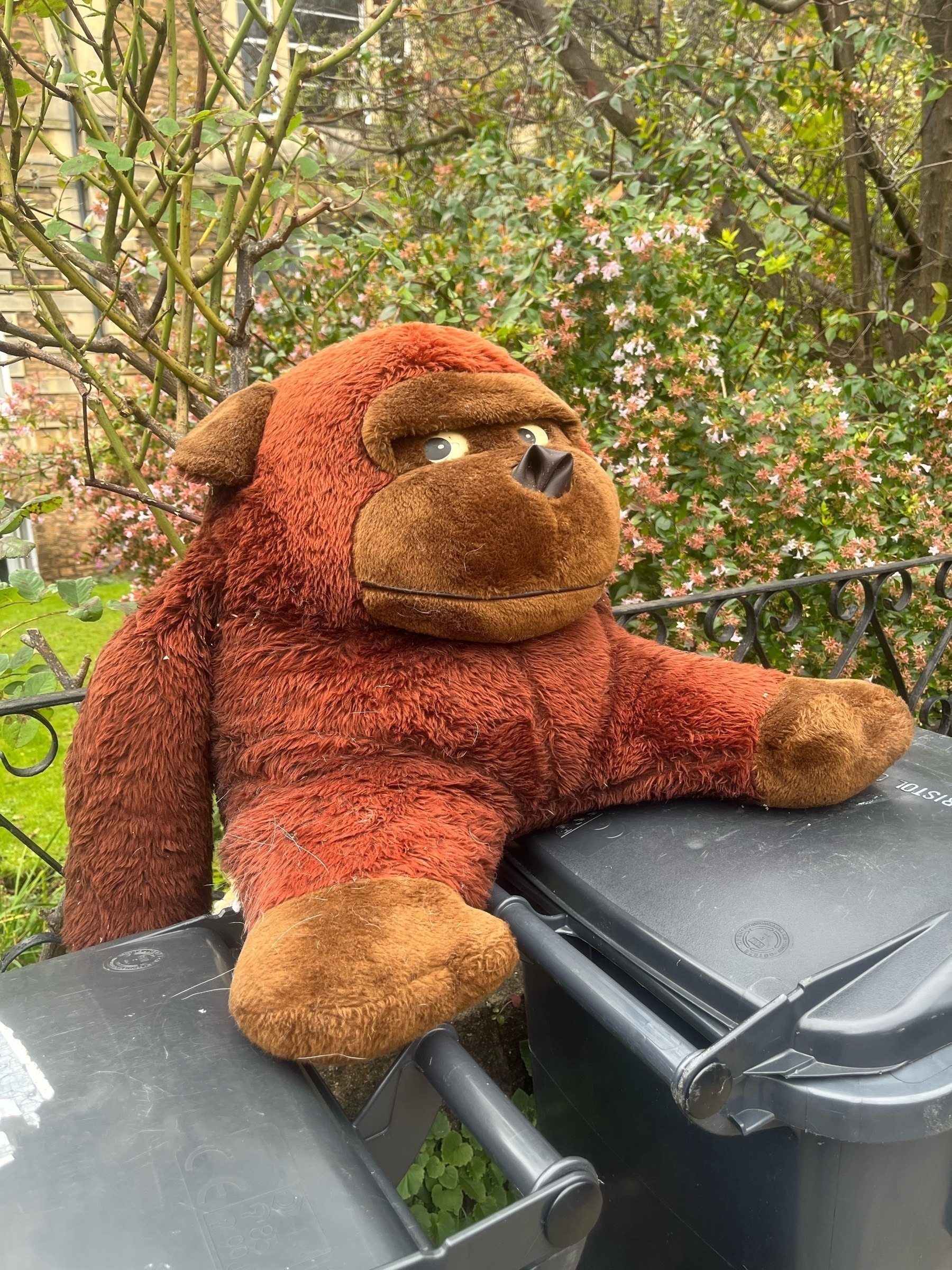 A stuffed cuddly toy monkey, coloured shades of tan and brown, sitting on top of trash cans.