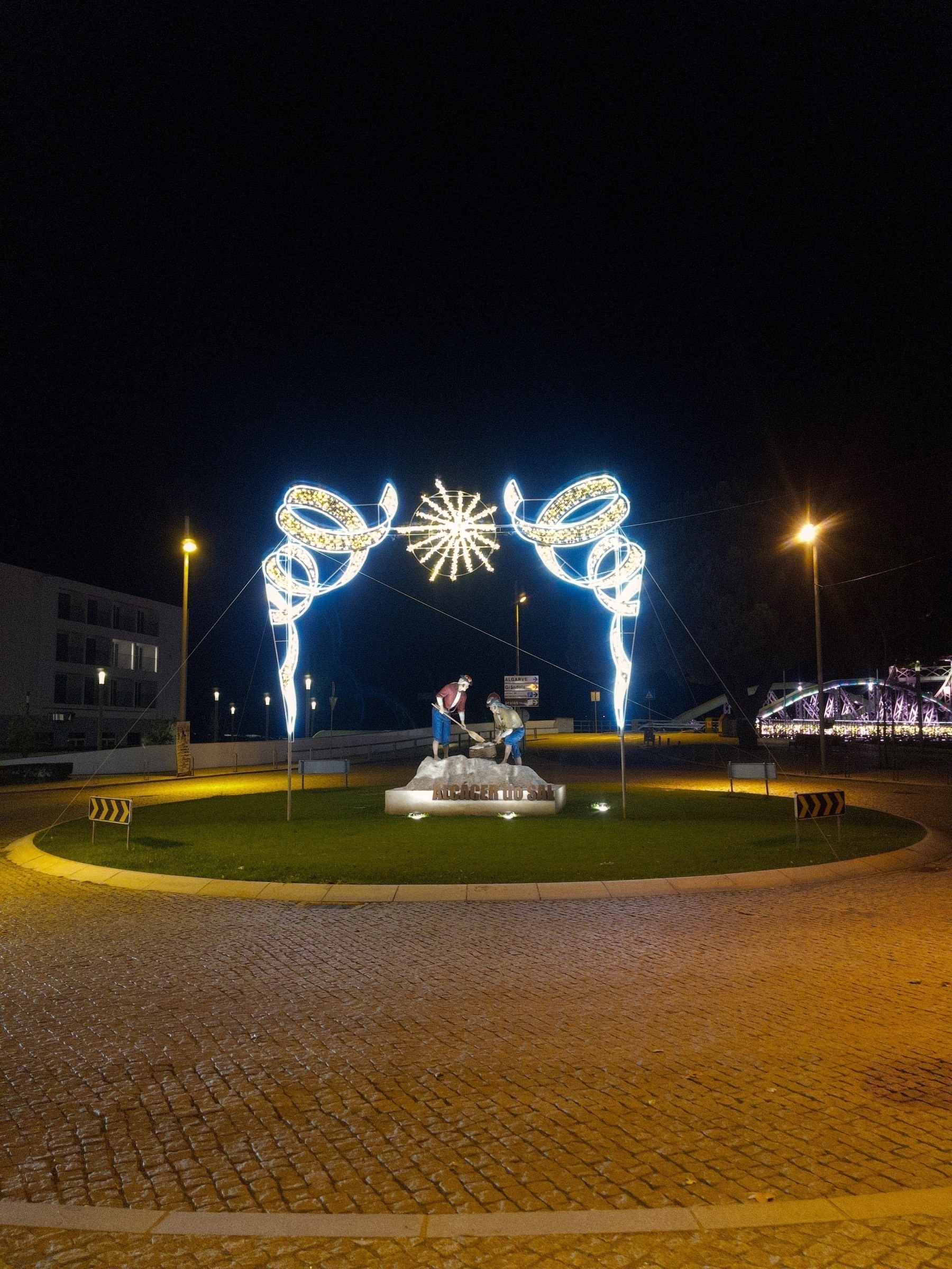 Festive and Decorative street lighting above a statute of men digging for salt by the town name Alcácer do Sal.