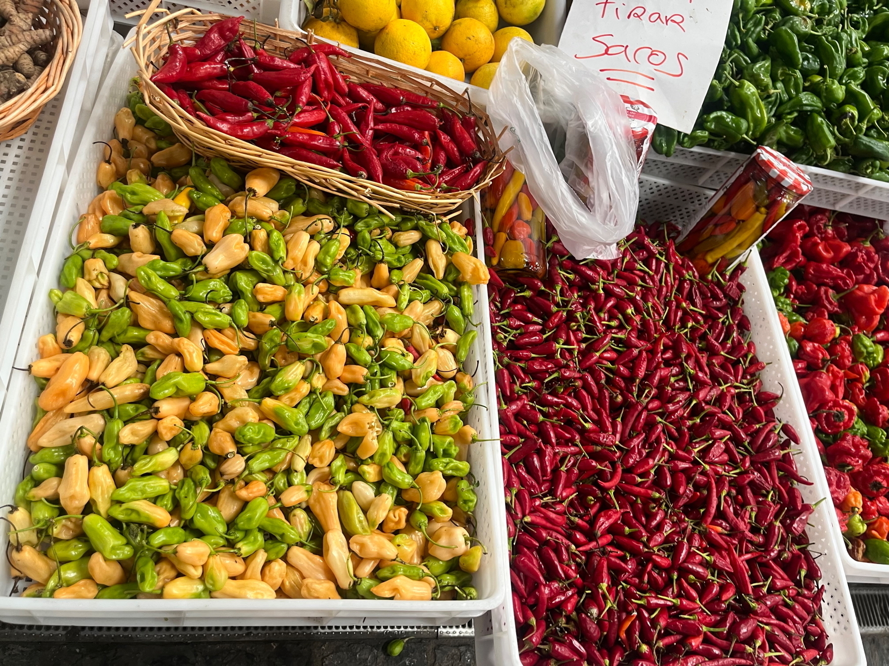 Assorted peppers in a market, including green, orange, yellow, and red varieties.