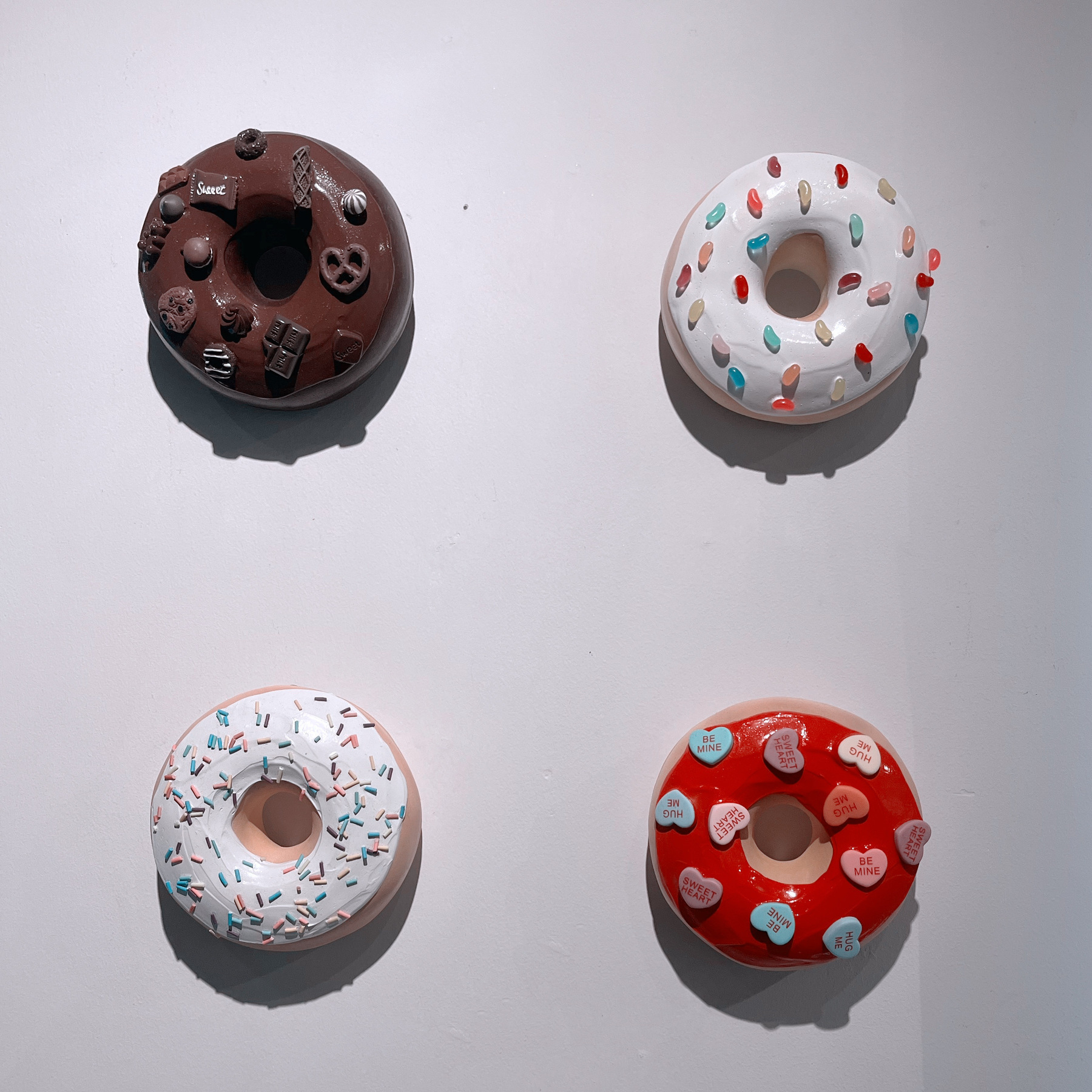 Auto-generated description: Four decorated doughnuts are displayed on a wall, varying in colors and toppings.