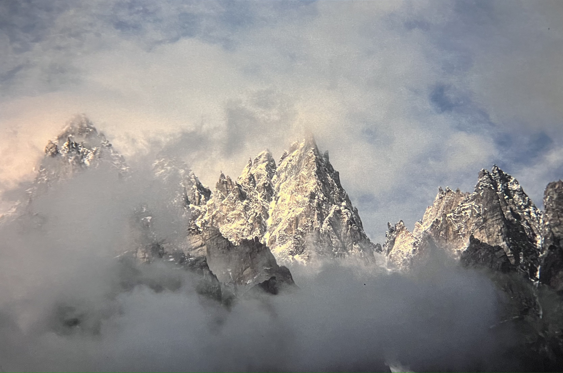 Grey, rugged, sharp mountain peaks with a little snow on them, surrounded by cloud