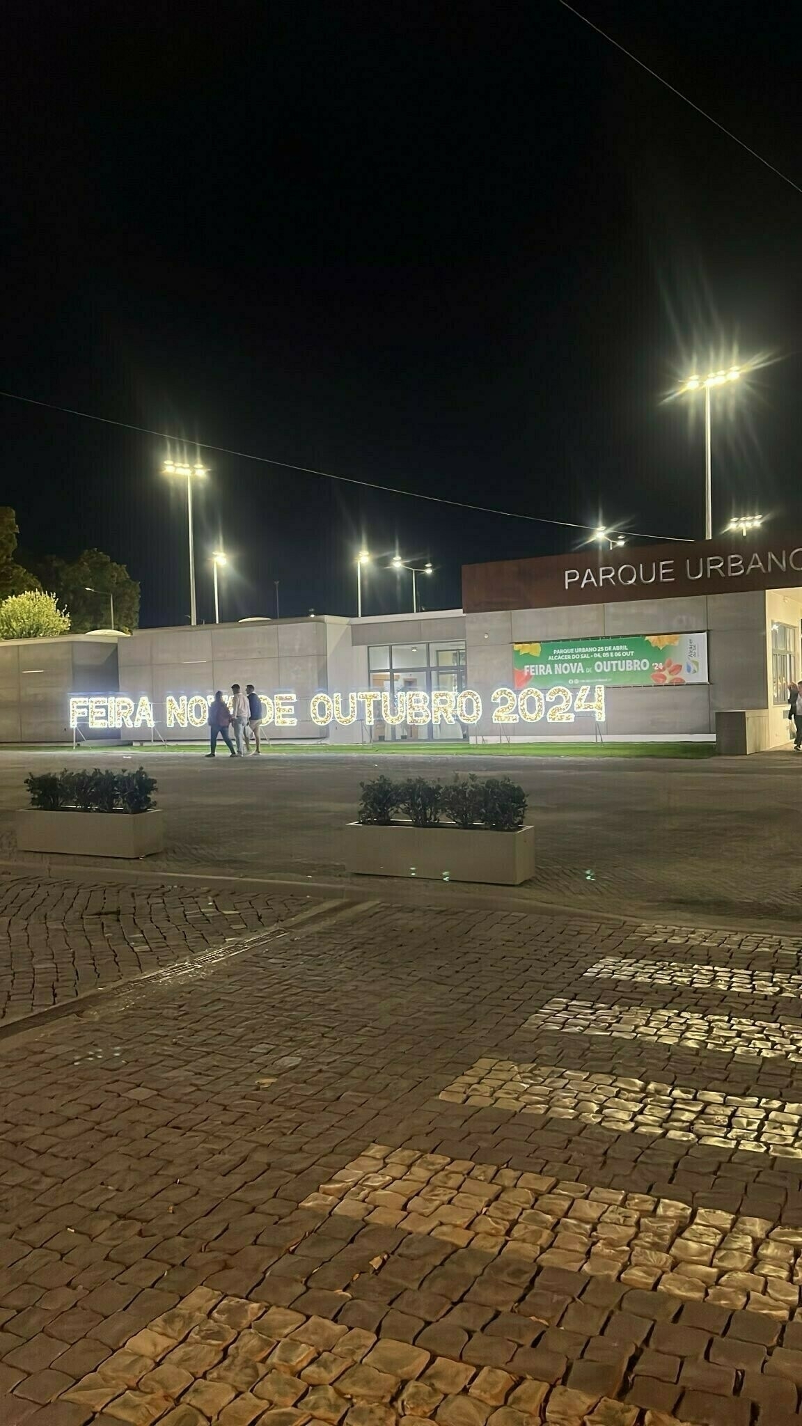 People walking in front of a lighted sign saying Feira Nova De Outubro 2024.