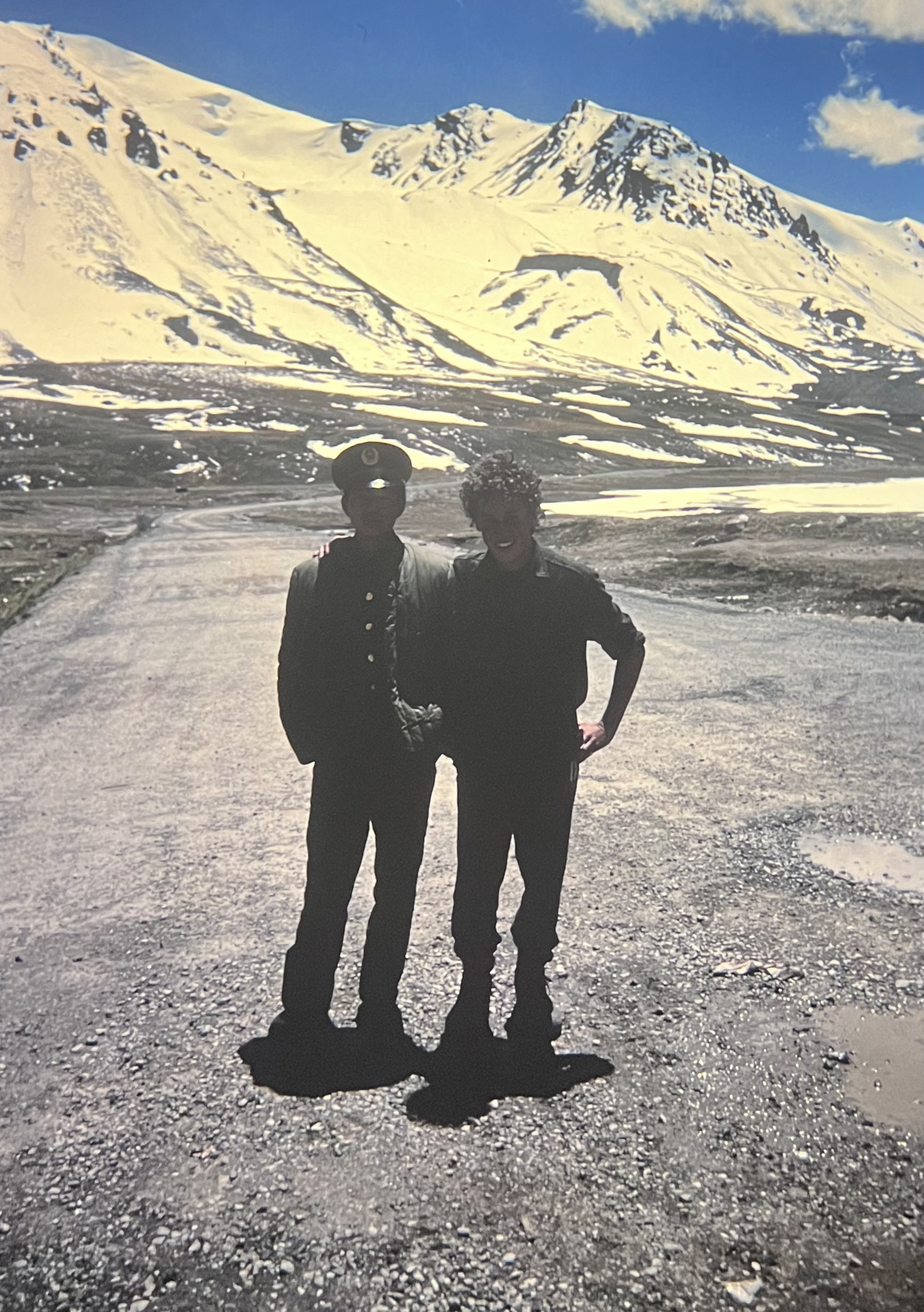 My arm around a Chinese guard at the Khunjerab pass. Standing on the highway, a single lane road, with the snow covered mountains behind us