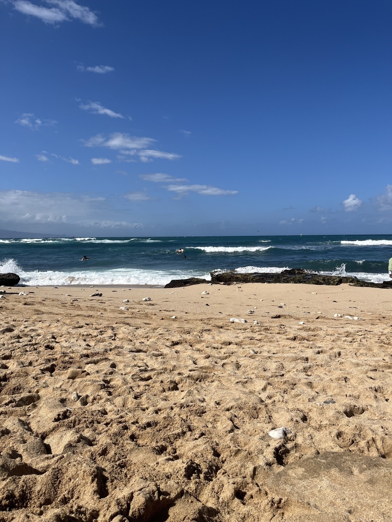 A sandy beach stretches toward a blue ocean with gentle waves under a clear sky.