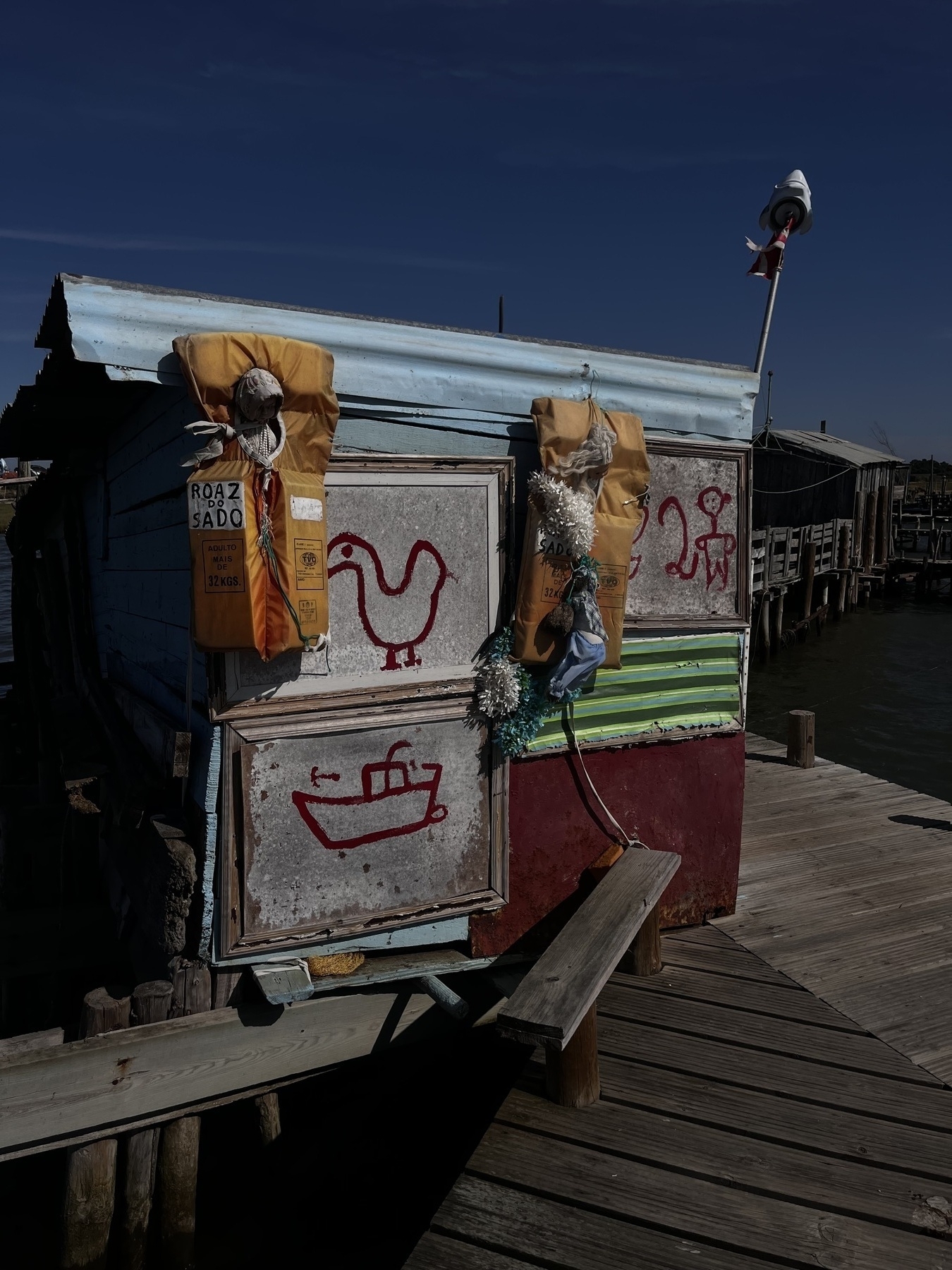 A colourful hand made wooden cabin with three child like drawings on the side and two life jackets