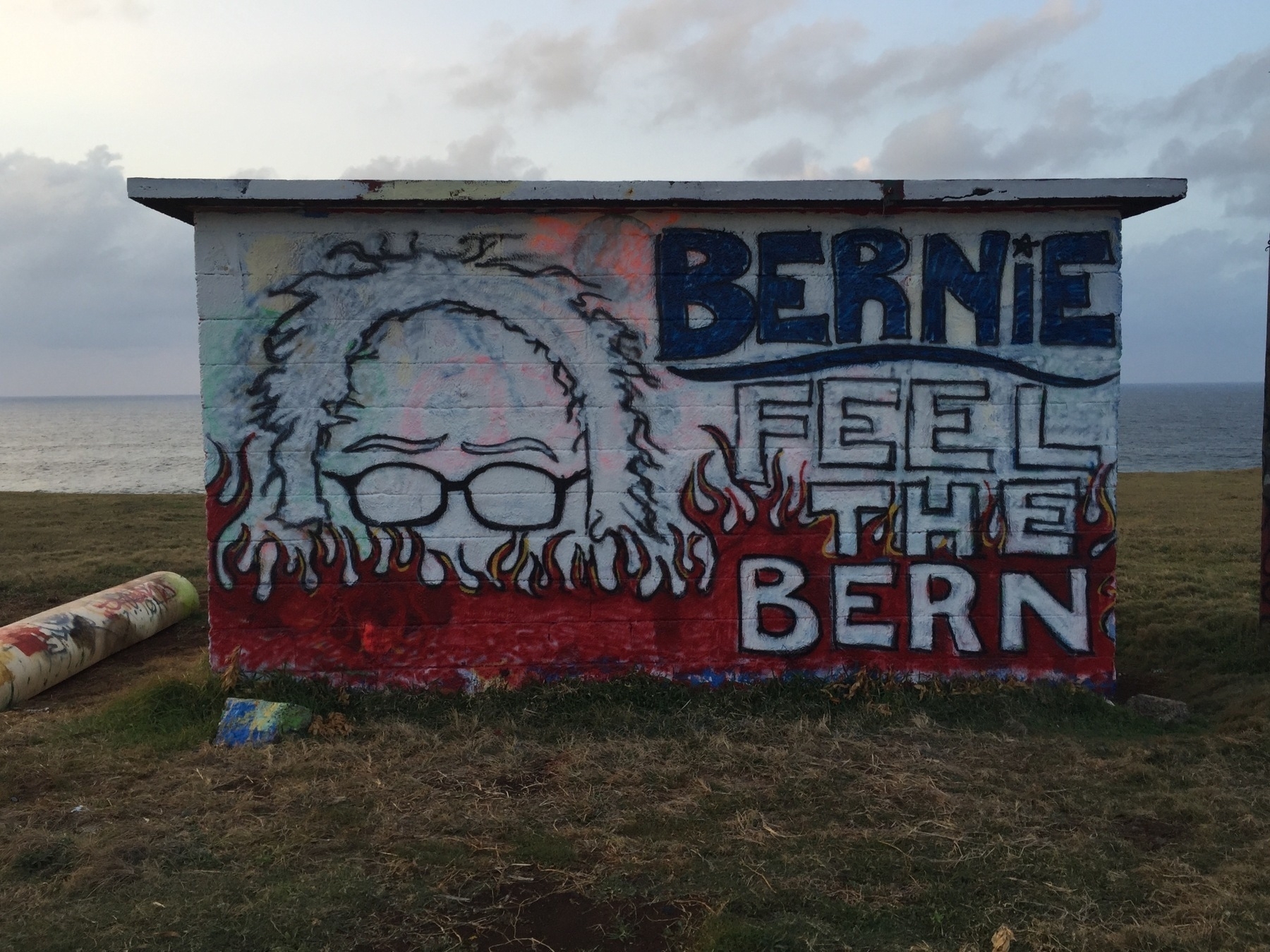 A mural features the phrase “Bernie Feel the Bern” alongside a stylized depiction of a person with glasses and wild hair, and flames rising up from the ground.