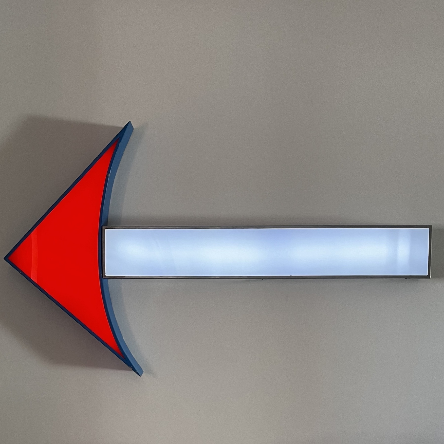 A large neon arrow made up of a red pointed end and white tail, all mounted on a white wall.