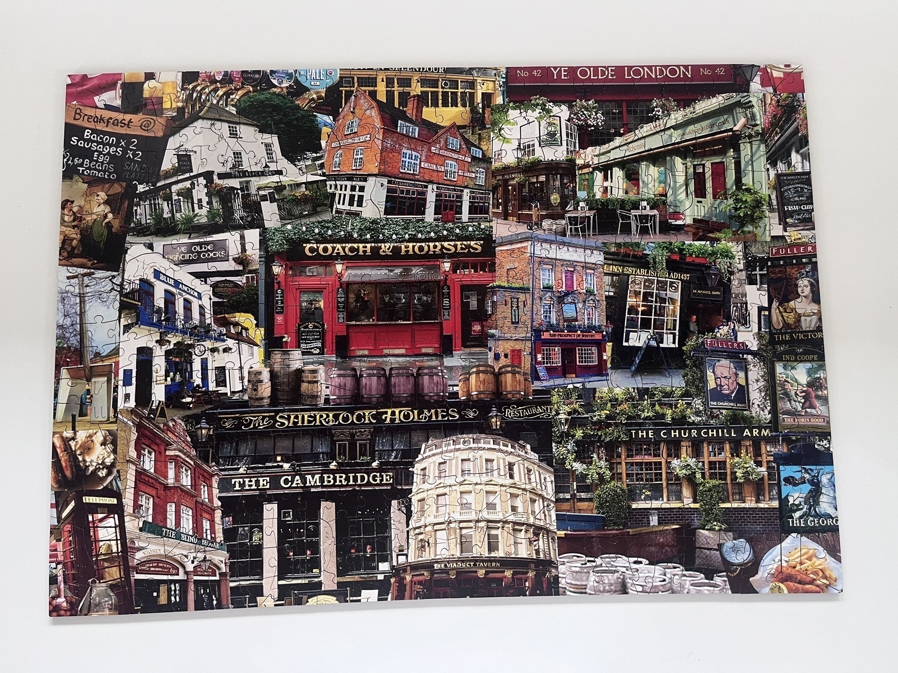 A completed jigsaw puzzle showing a colorful collage depicting various pub exteriors and signs from around Britain, each with intricate architectural details and vibrant storefronts.