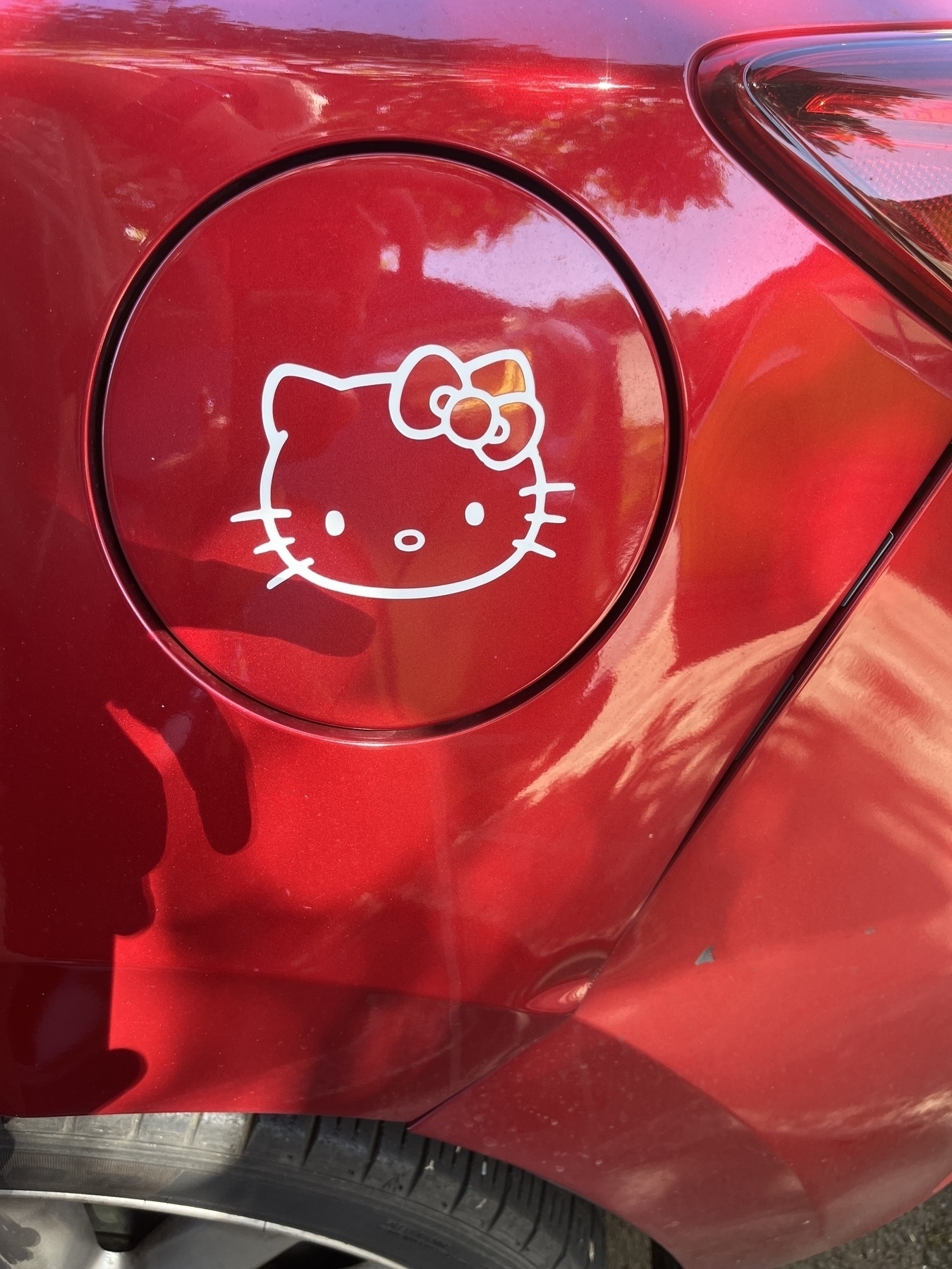 A Hello Kitty sticker is placed on the fuel cap area of a red vehicle.