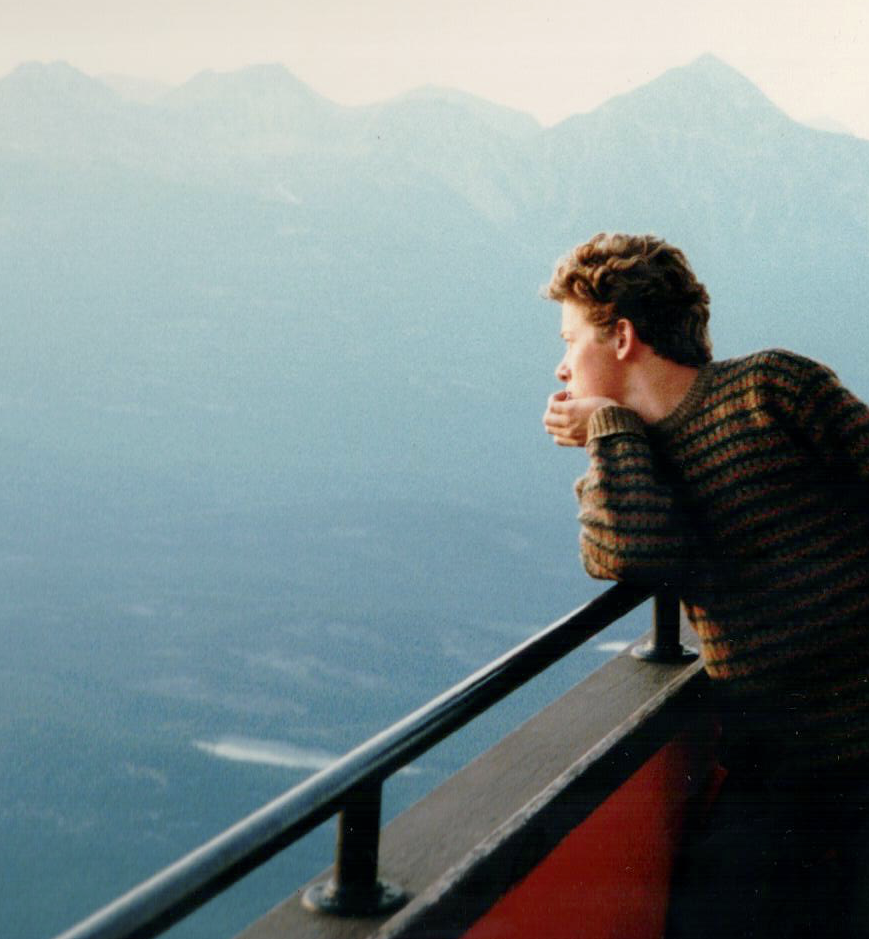 A person, myself, is leaning over a railing, gazing at a scenic, mountainous landscape in the distance.