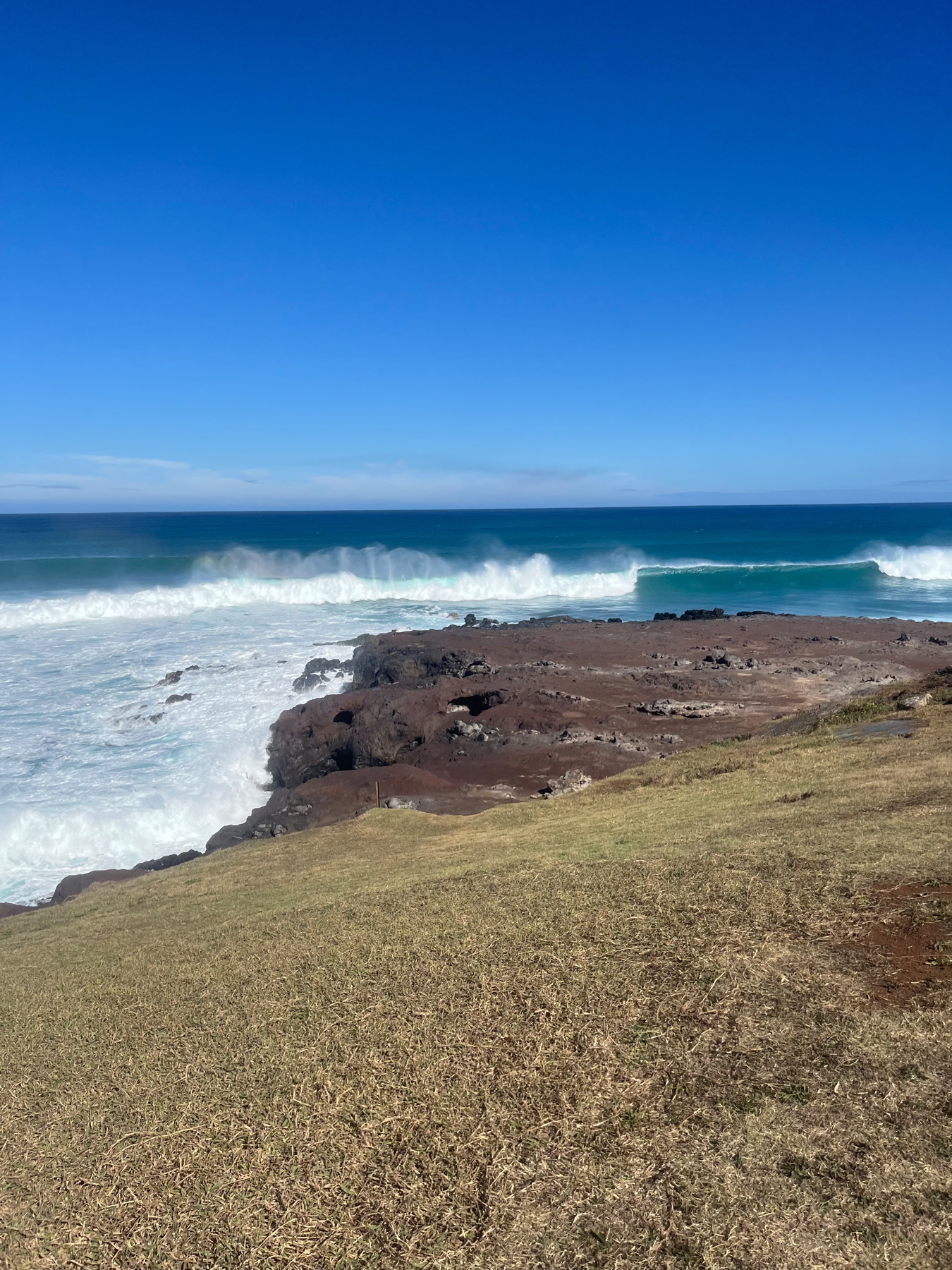 An ocean scene with waves crashing against rocky cliffs under a clear blue sky.