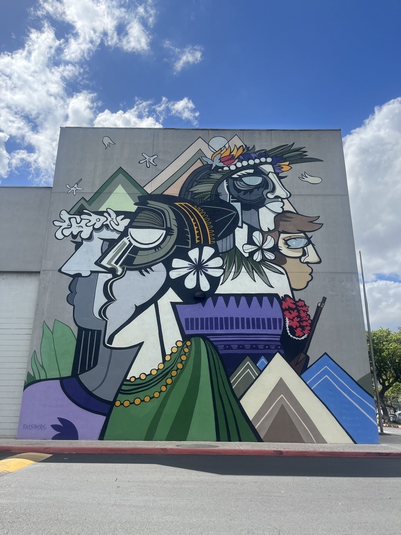 A vibrant mural depicting abstract human faces adorned with floral motifs and geometric shapes covers the side of a building.