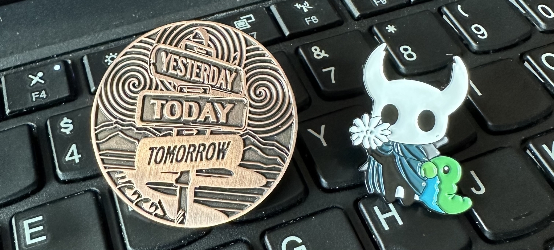 Circle eggy pin says “yesterday today tomorrow” and hollow knight pin holding white flower and grub. 