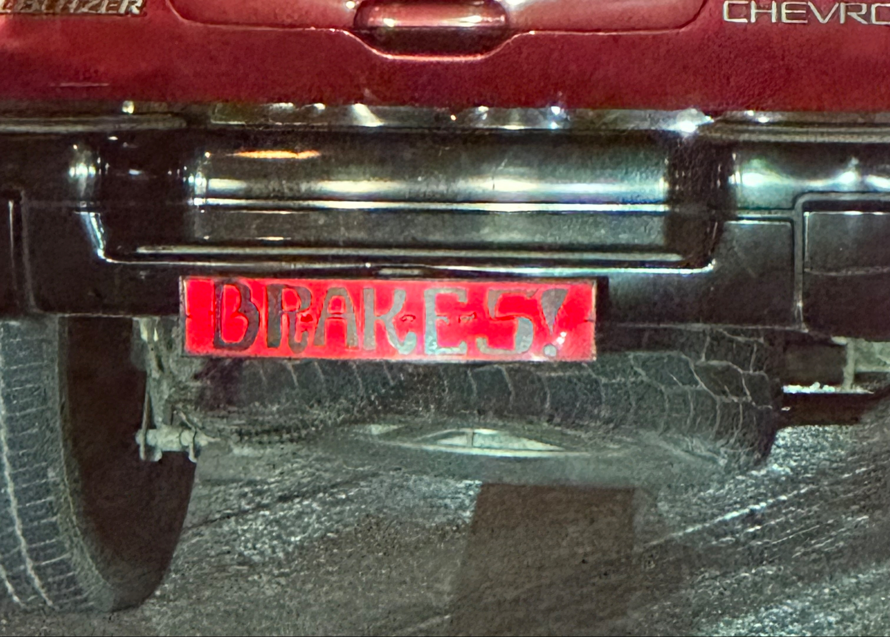 Rear view of a red Chevrolet Blazer with a custom license plate that reads “BRAKES!” displayed in red lettering on a reflective background.