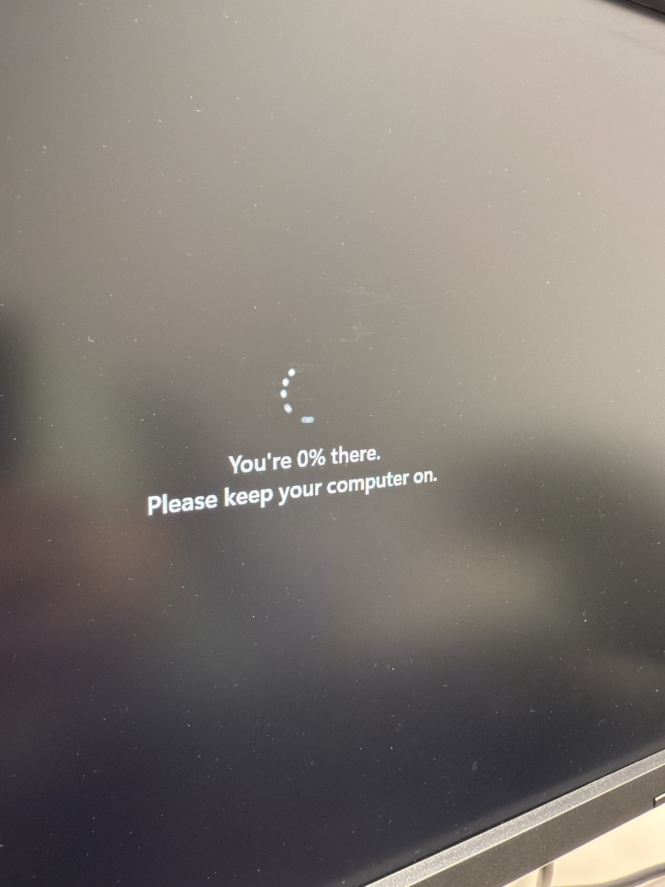 A computer screen displays a message reading, "You're 0% there. Please keep your computer on," along with a loading circle.