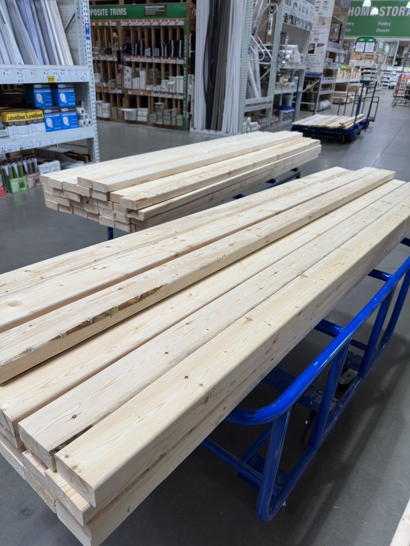 Auto-generated description: A stack of wooden planks is neatly arranged on blue carts in a home improvement store aisle.