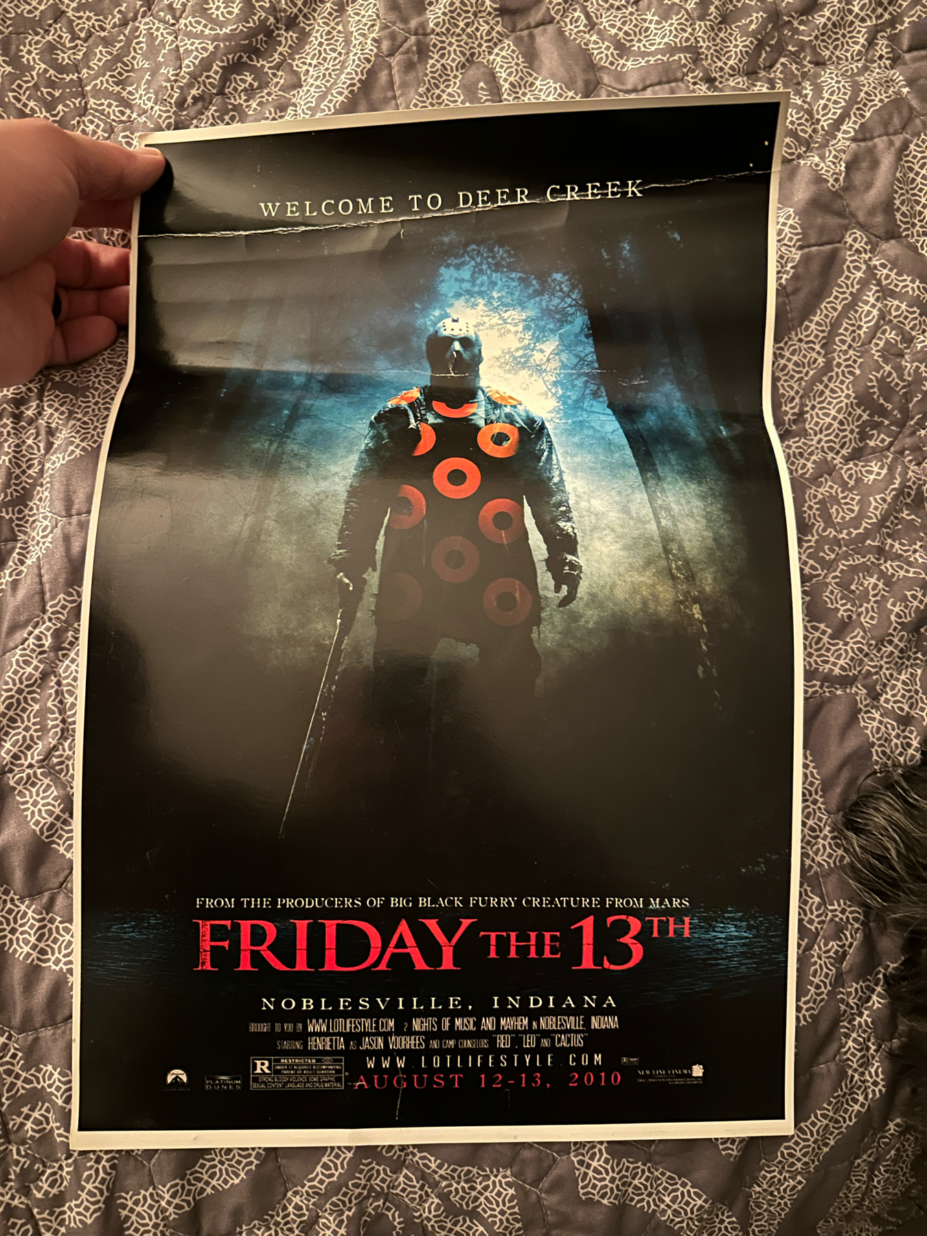 A poster for an event titled “Welcome to Deer Creek,” mimicking a “Friday the 13th” horror movie theme, featuring a person in the center dressed as the iconic character Jason Voorhees standing in a misty, wooded area.