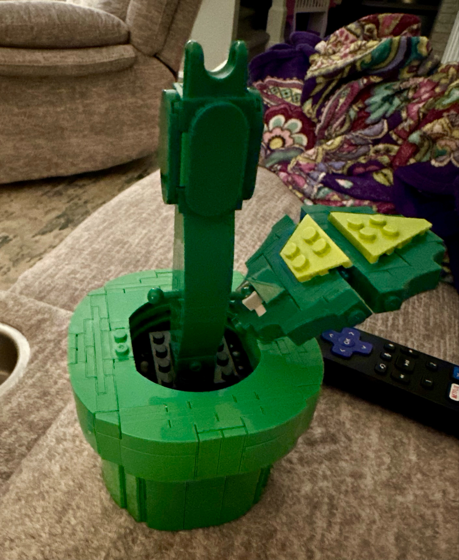 A constructed Lego model resembling a green piranha plant from the “Super Mario” series, displayed on a carpeted floor.