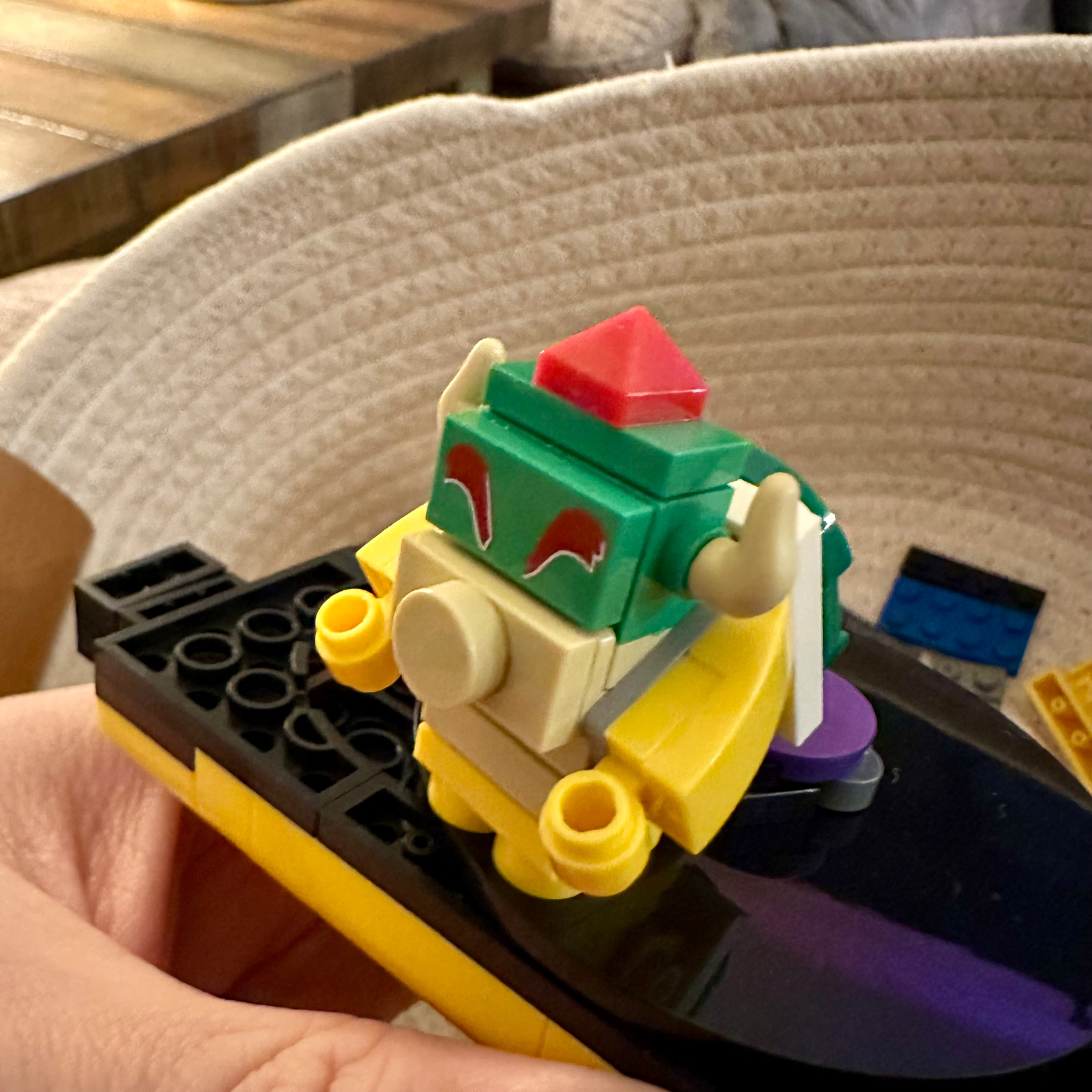 A LEGO model resembling a dinosaur head with red eyes is held over a table, with a hand partially visible in the frame.