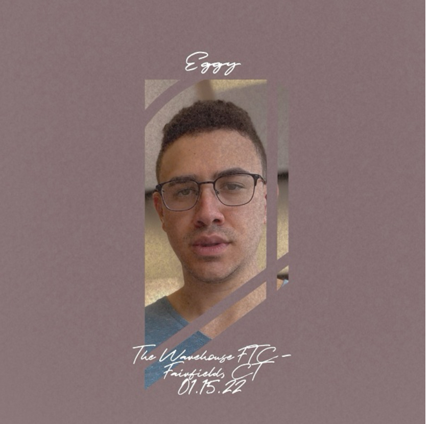 The image is a promotional graphic containing a portrait of a man with short hair and glasses centered within a geometric frame. Above the frame is the handwritten text “Eggy,” and below there’s additional text reading “The Warehouse FTC - Fairfield CT 