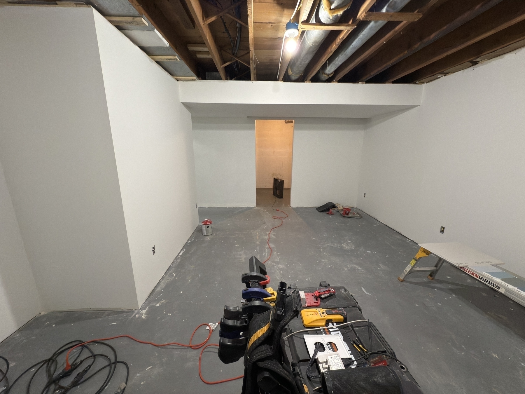 A room under construction features exposed ceiling beams, a partially finished floor, and tools on a cart in the foreground.