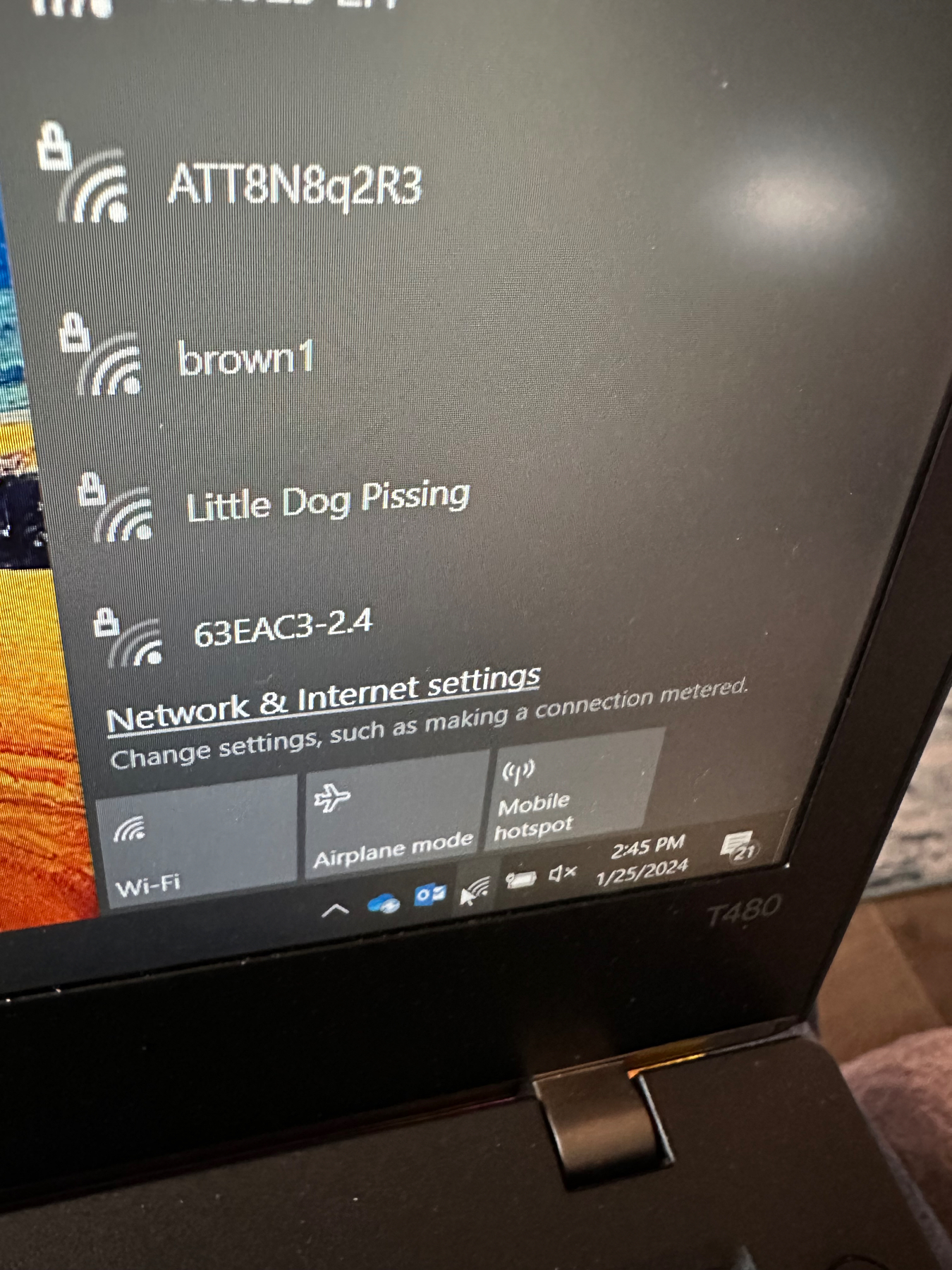 A laptop screen displaying a list of Wi-Fi network names with one highlighted as ‘Little Dog Pissing.’ Also visible are icons for Wi-Fi, Airplane mode, and Mobile hotspot, along with the time ‘2:45 PM’ and the date