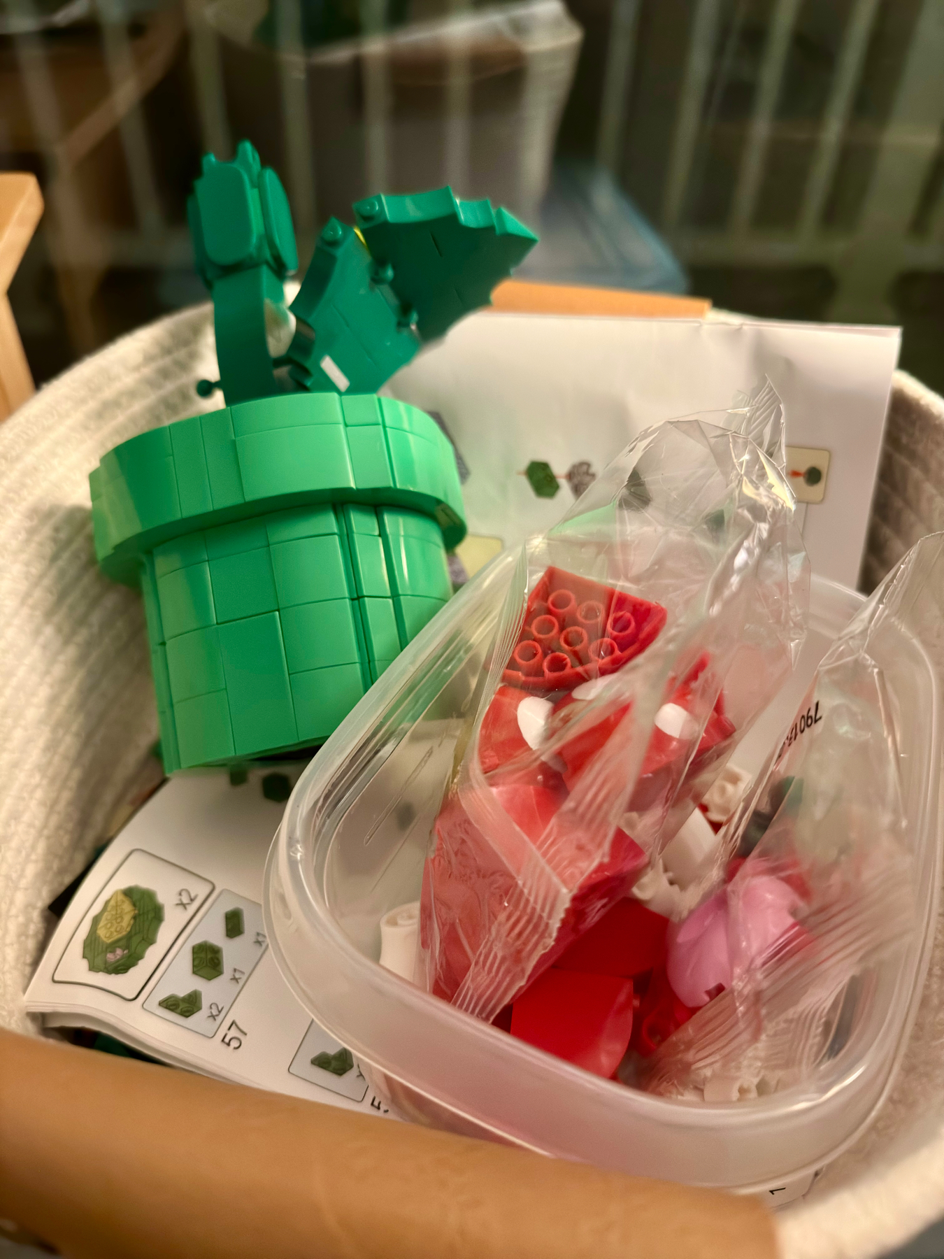 A partially completed LEGO flower bouquet, with a green brick-built vase and some flower stems, alongside sealed bags of LEGO pieces and an instruction manual.