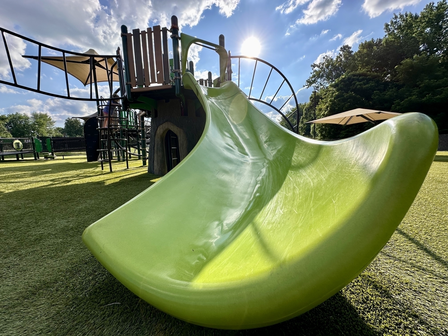 A vibrant green slide is part of a playground under a sunny sky with some clouds.