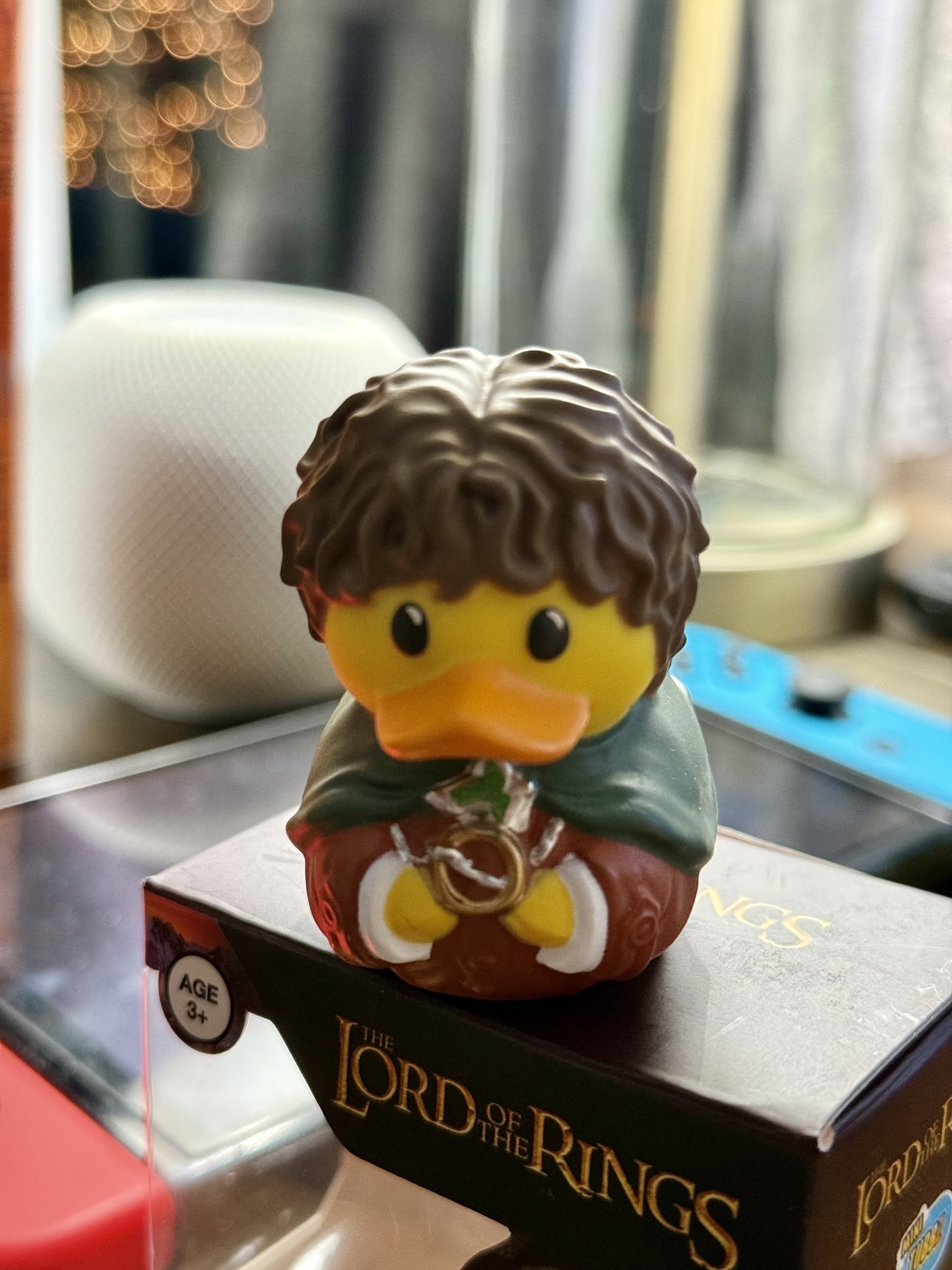 A rubber duck styled as a character from "The Lord of the Rings" holds a ring while standing on a themed box.