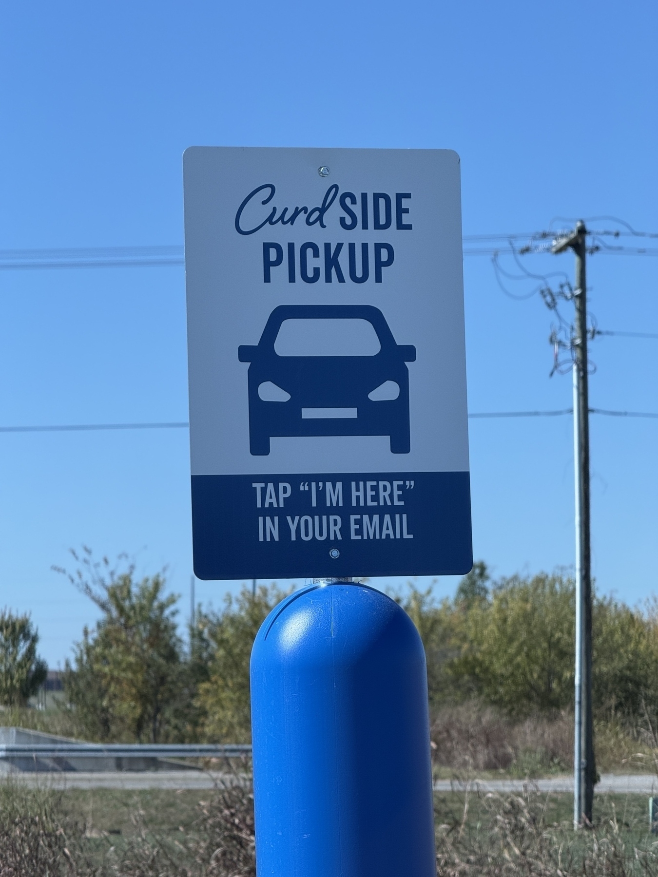 A sign indicates a location for curbside pickup, featuring a car icon and instructions to "Tap 'I'm Here' in your email."