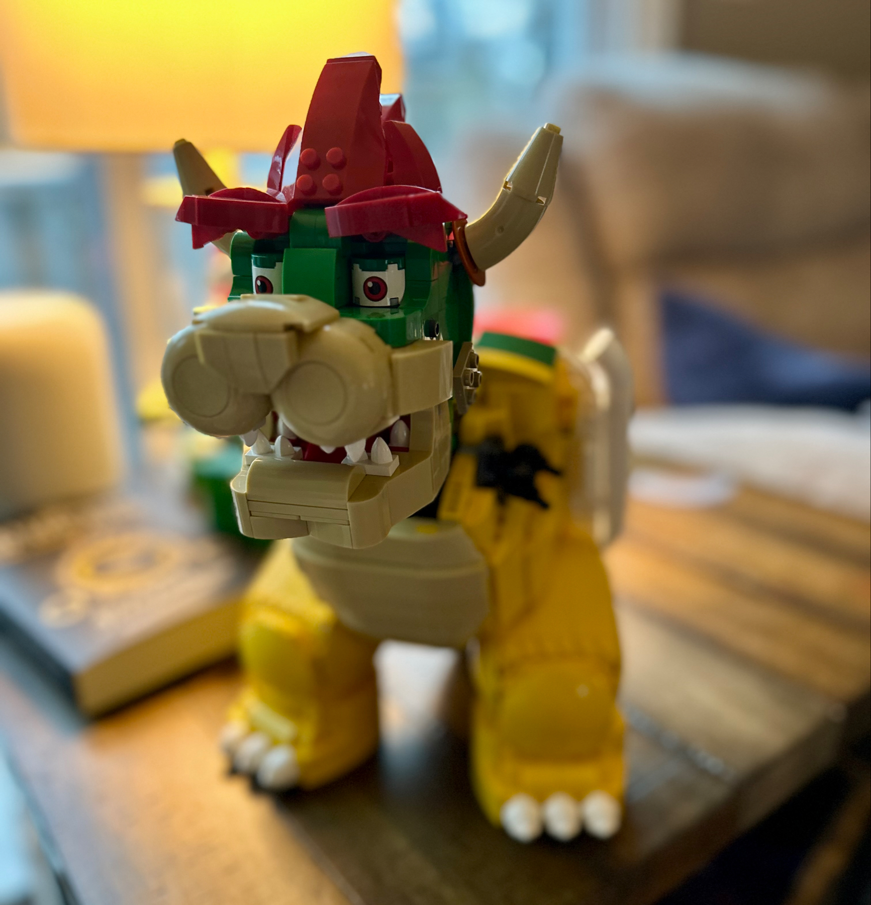 A LEGO Bowser model of a dinosaur with red spikes, green head, white teeth, and yellow body displayed on a wooden surface.