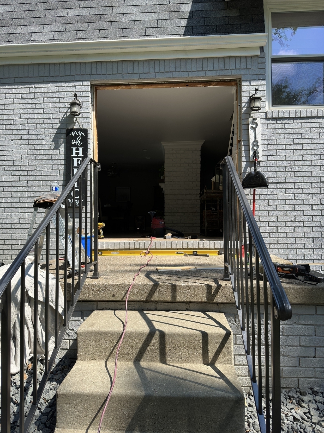 A set of concrete stairs with black metal railings leads to a doorway under renovation, with construction tools and materials visible in the background.