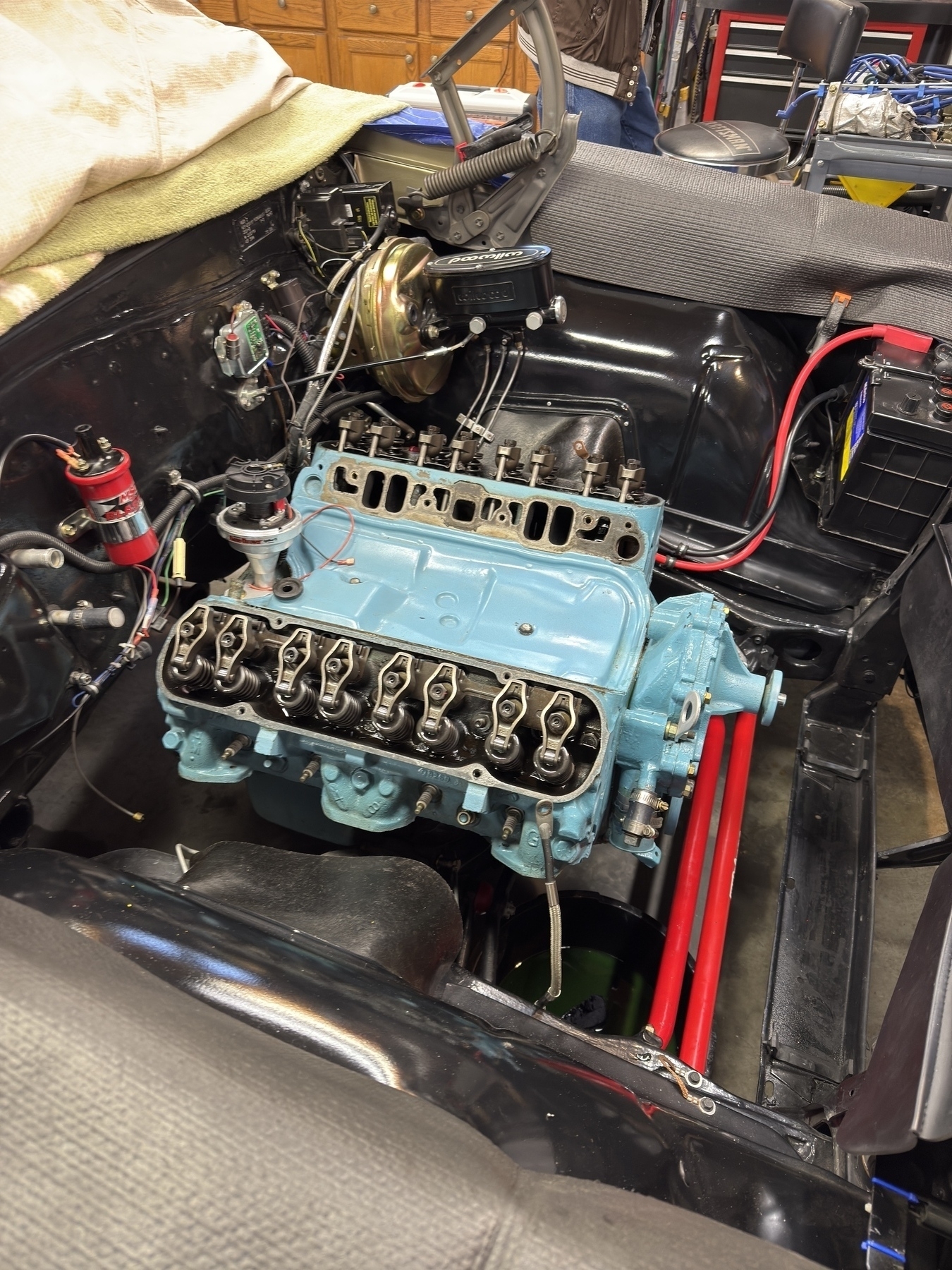 A classic car's engine bay is shown, featuring a partially assembled light blue engine with visible wiring and components.