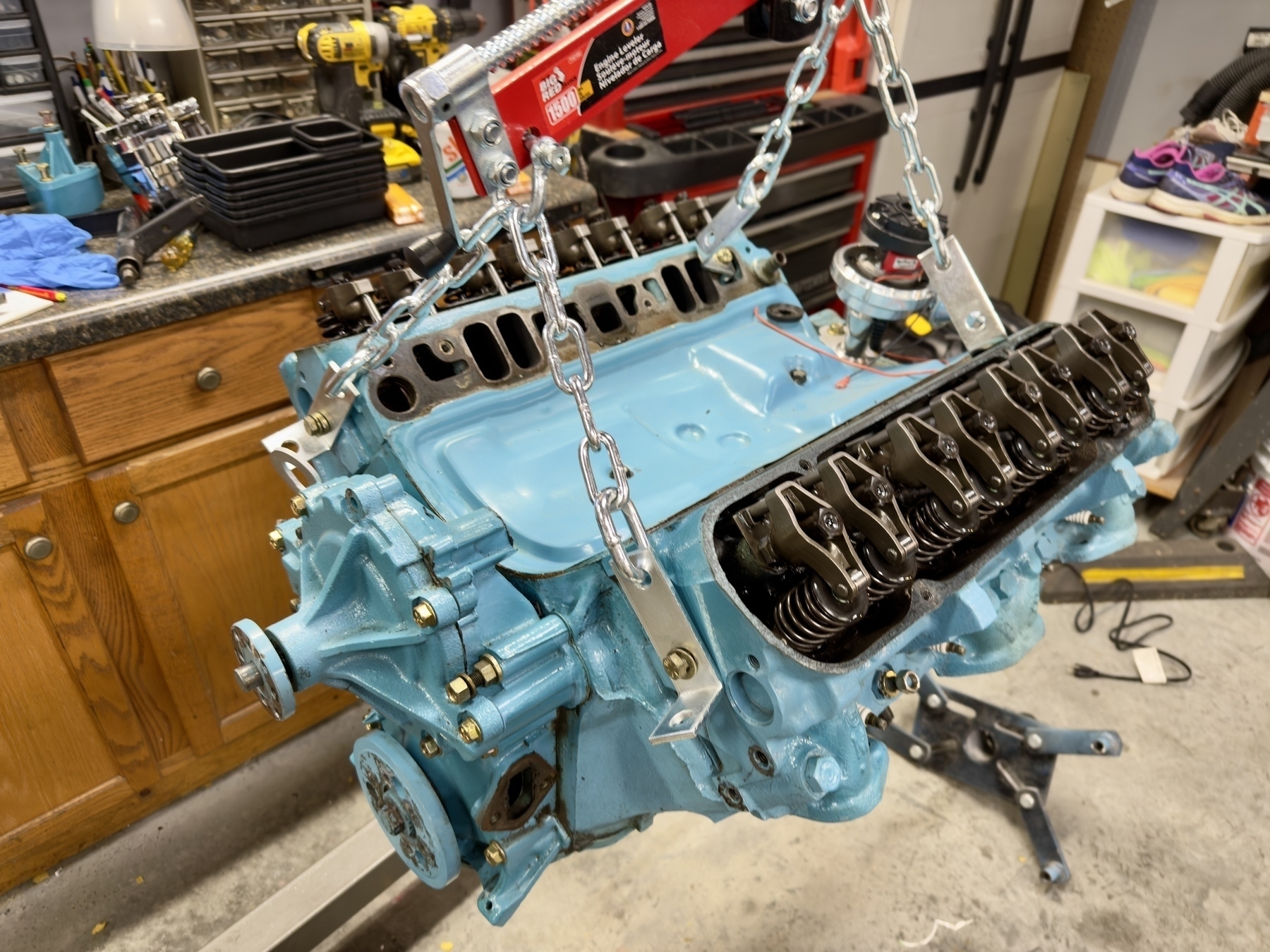 A blue engine block is being supported by a hoist in a garage workspace.