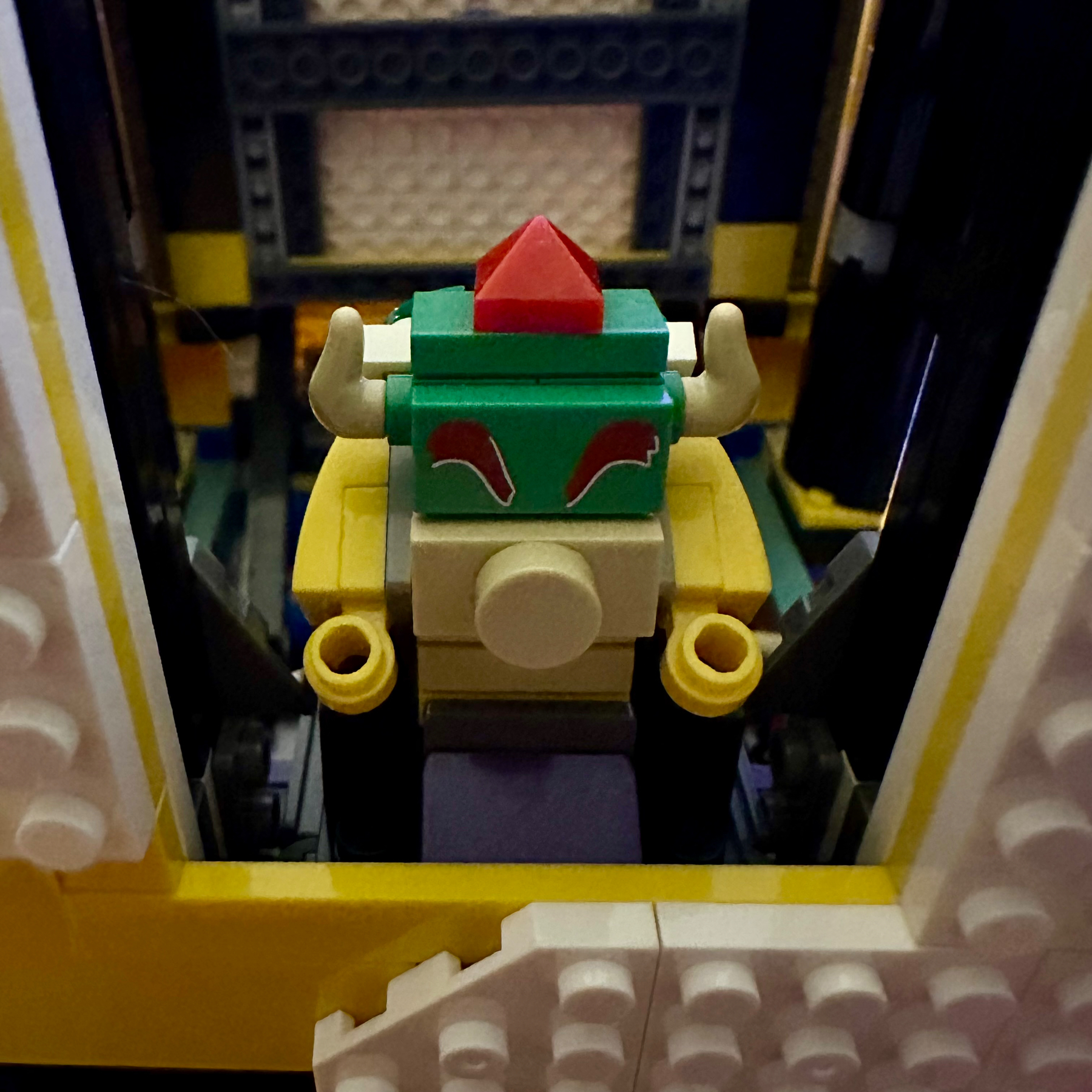 A close-up photo of a LEGO figure with horns and a red jewel on its head, resembling a character or deity, set within a blocky interior structure.