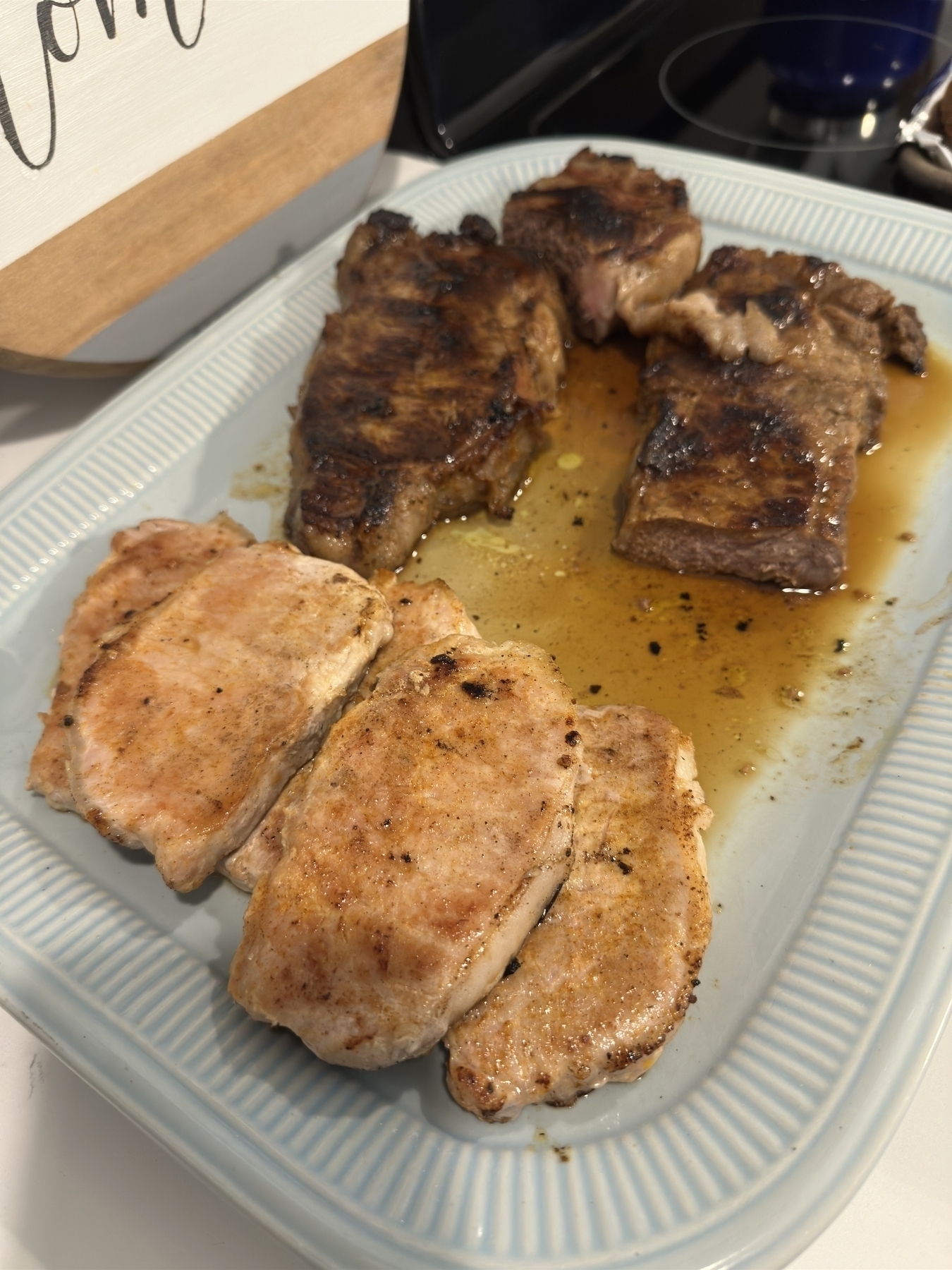 A blue plate with several pieces of grilled meat, some browned and seasoned, sits on a surface next to a cutting board.