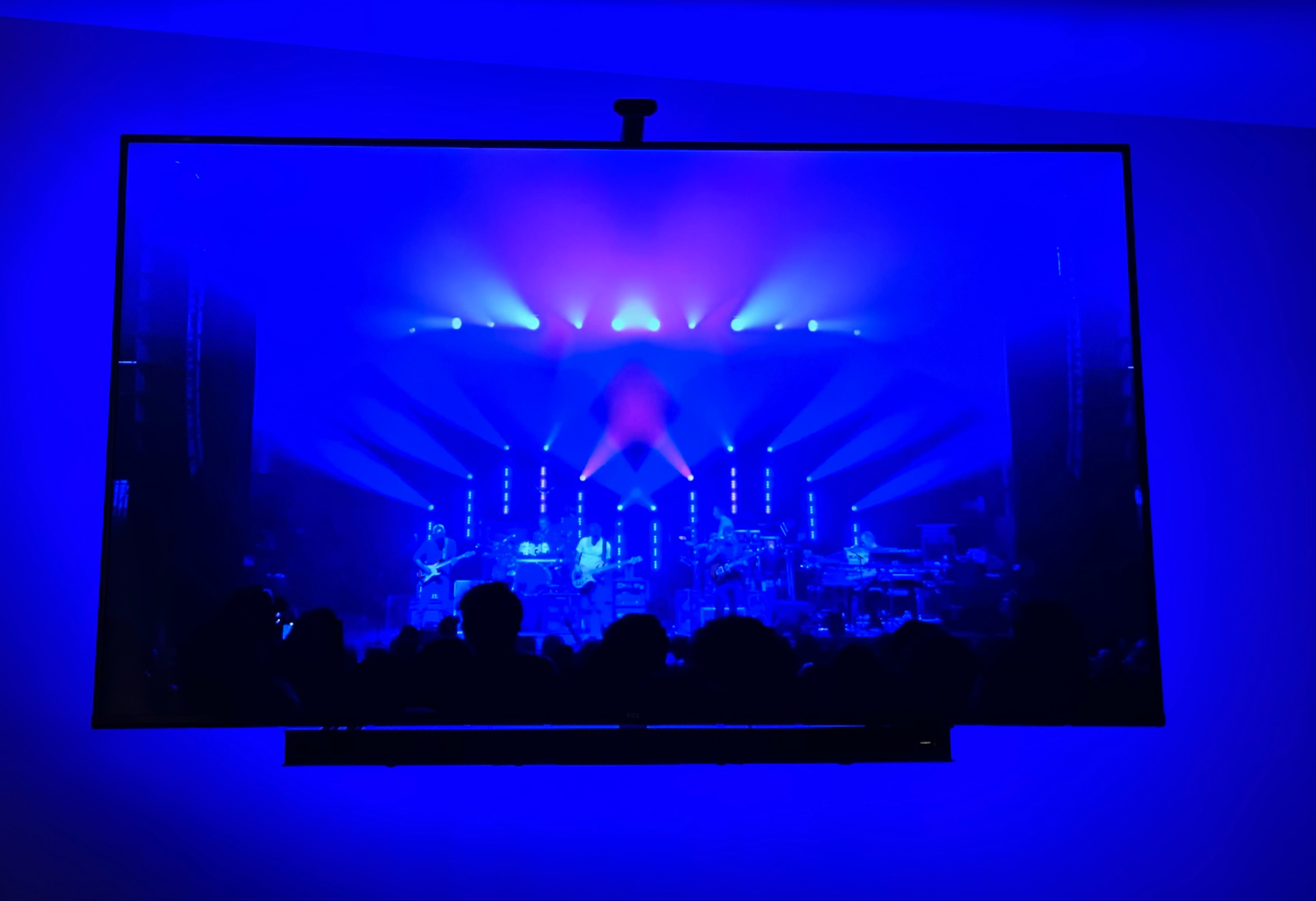 A concert scene displayed on a TV with colorful stage lighting, showing silhouettes of the audience and performers.