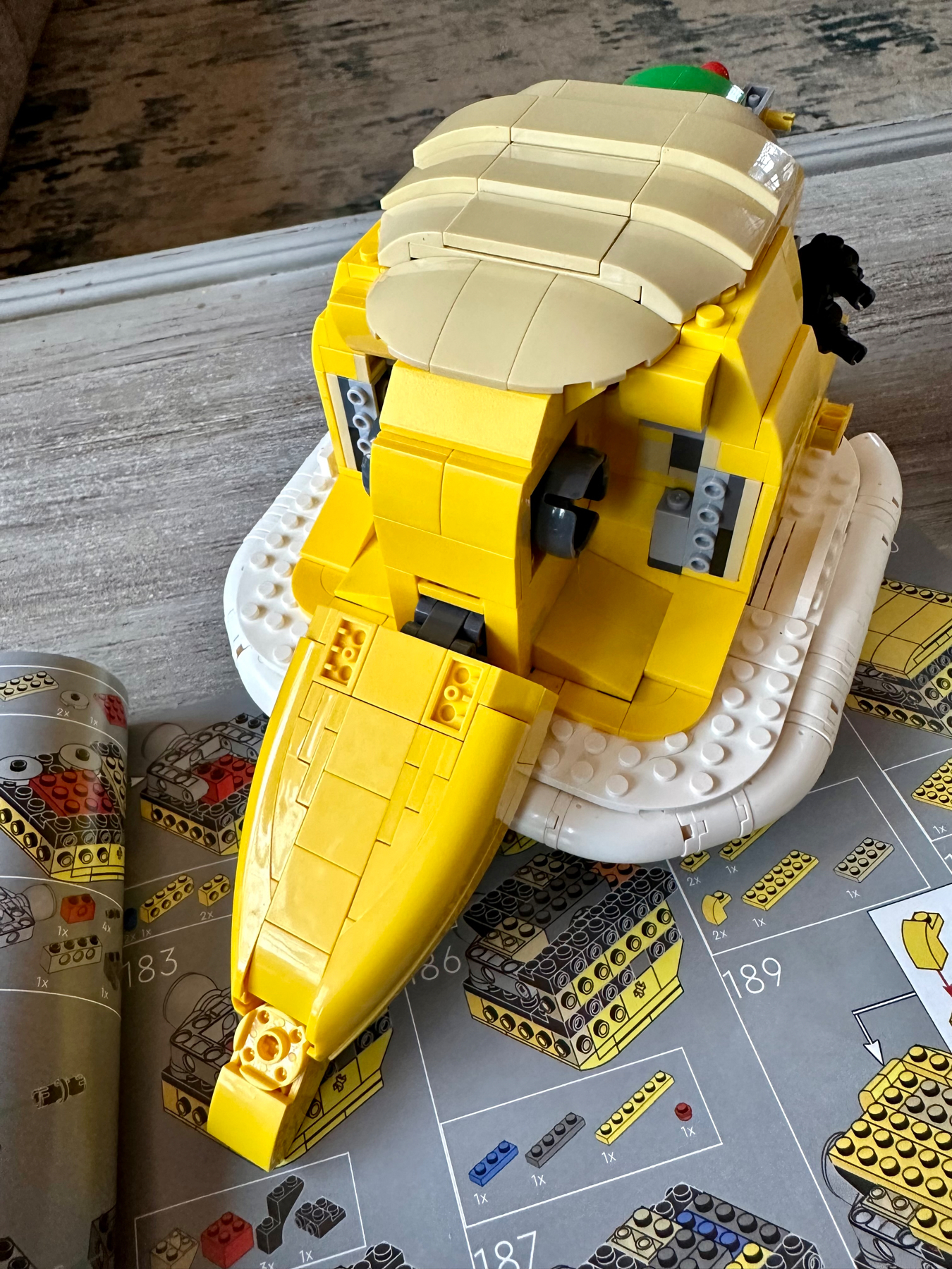 A partially assembled Lego set resembling the head of a lion lays on top of an instruction manual, with bricks in yellow, white, and black colors.